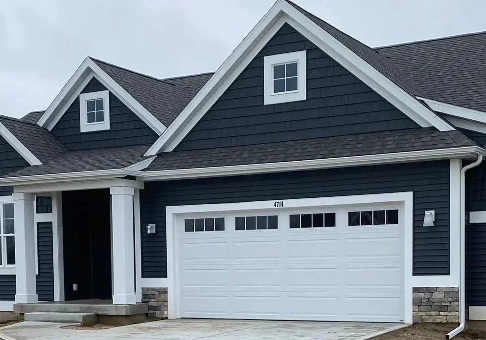 Front view of a modern black house with white trim, white garage door, and stone accents, during daytime.