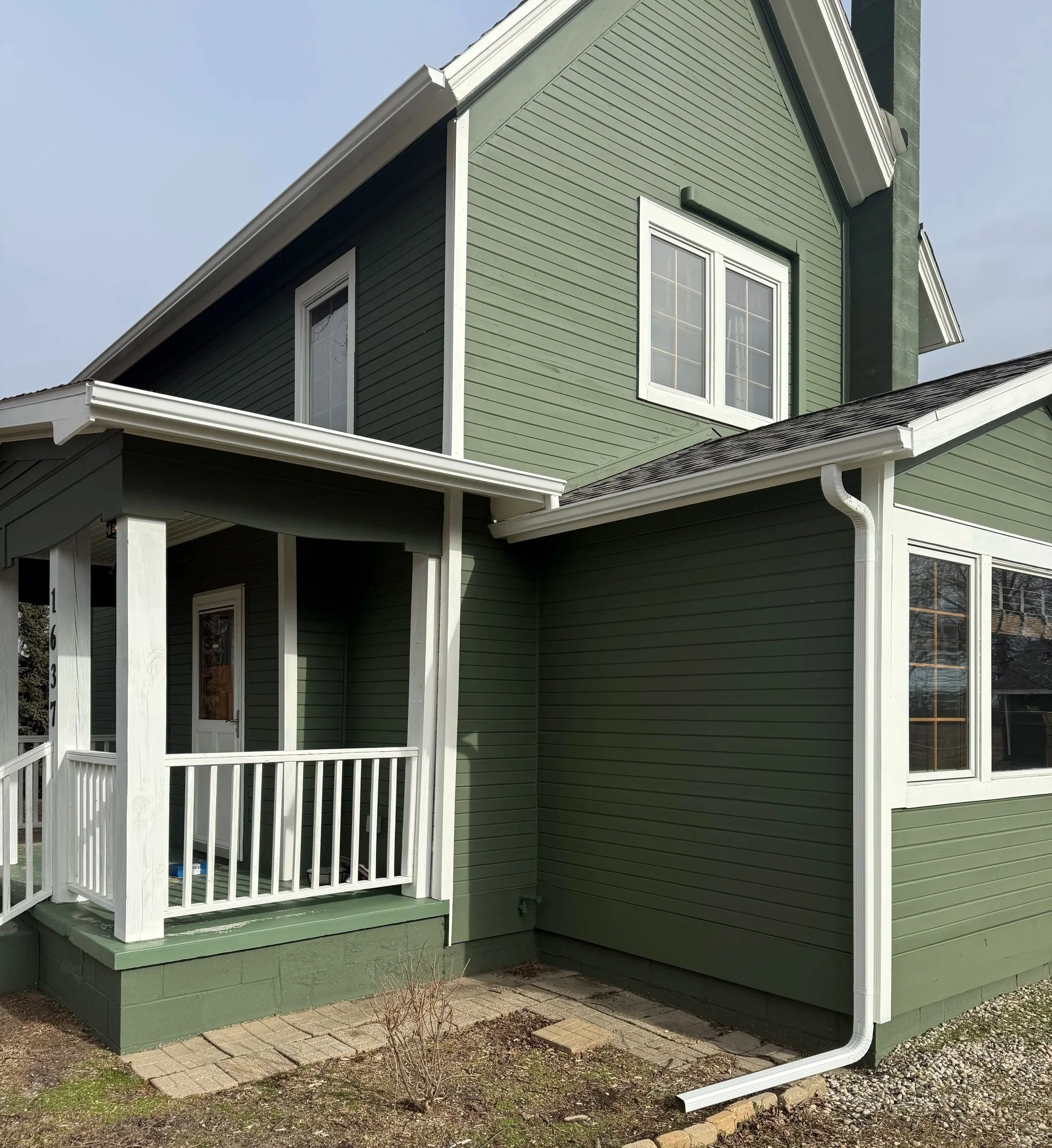 A two-story green house with white trim and a small front porch with white railing.