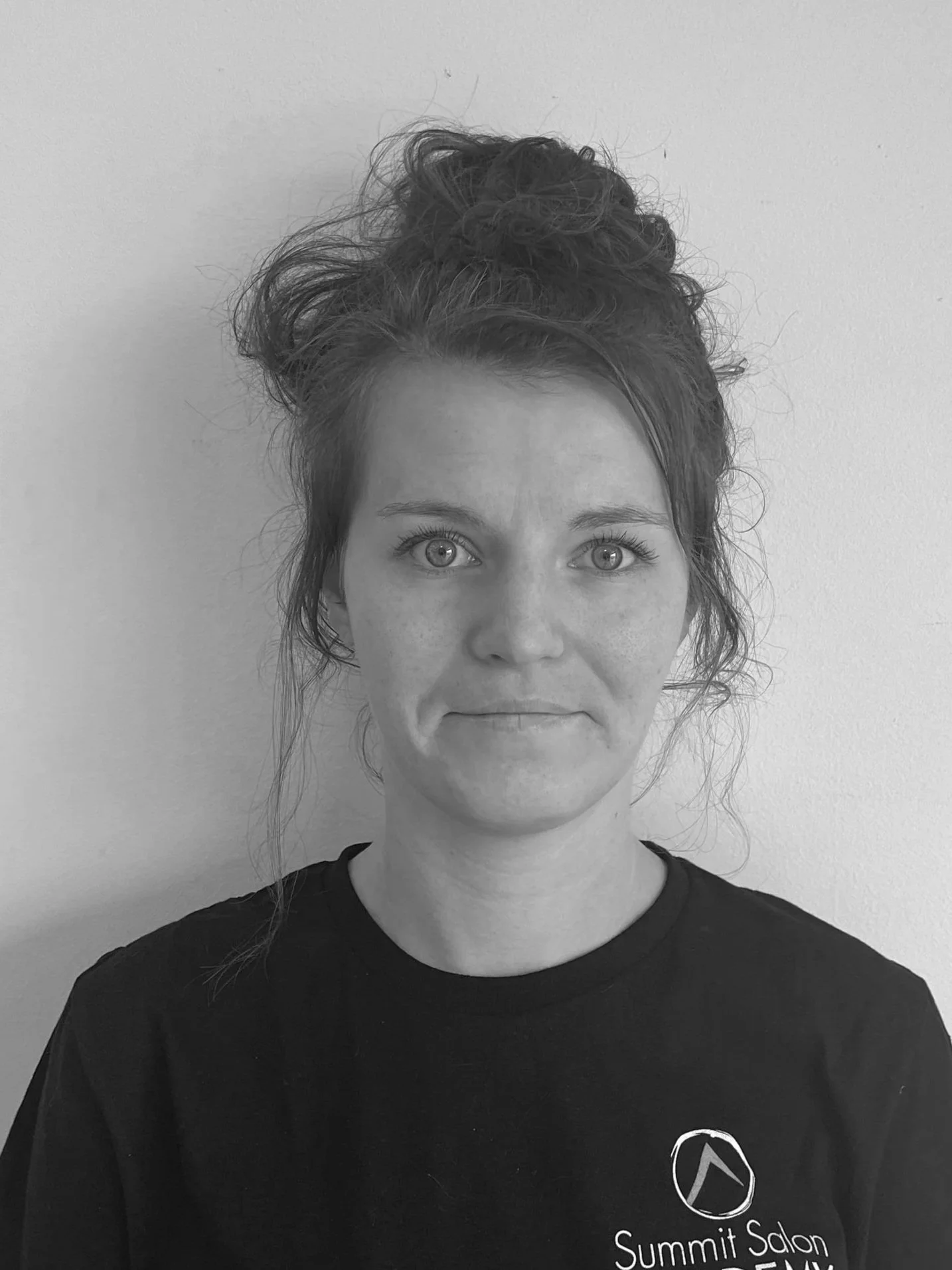A smiling young woman with shoulder-length hair standing against a plain wall.