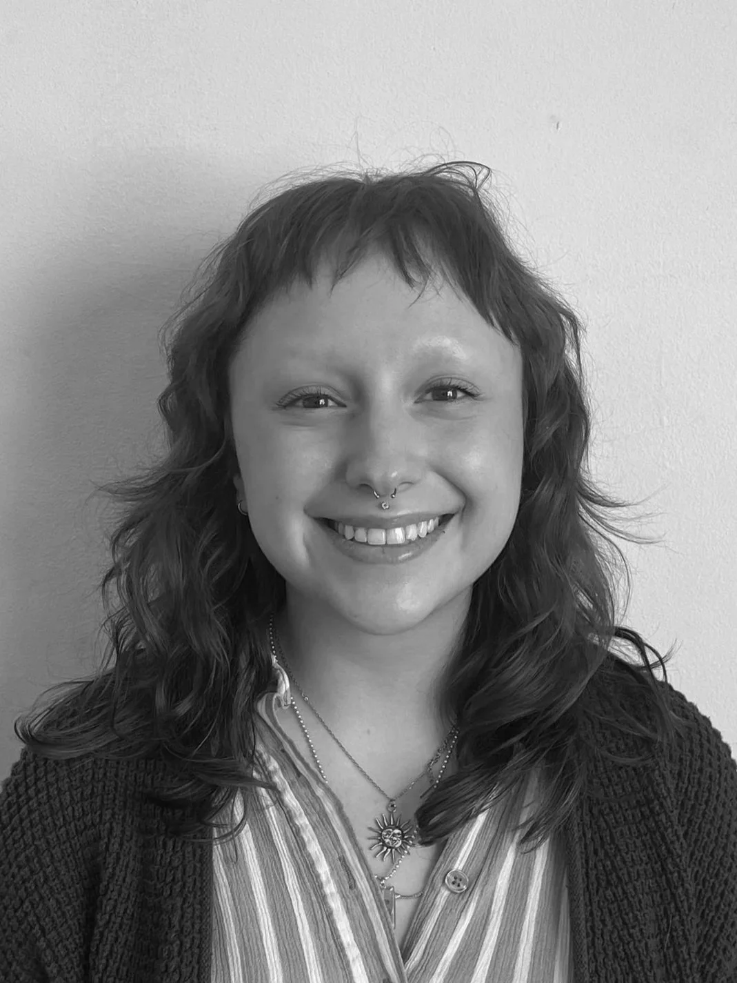 A young woman with long wavy hair, wearing a black hoodie with the logo 'Summit Academy' on it, smiling at the camera against a plain wall background.