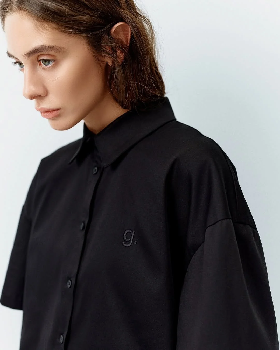 Woman in black button-up shirt with embroidered "g"