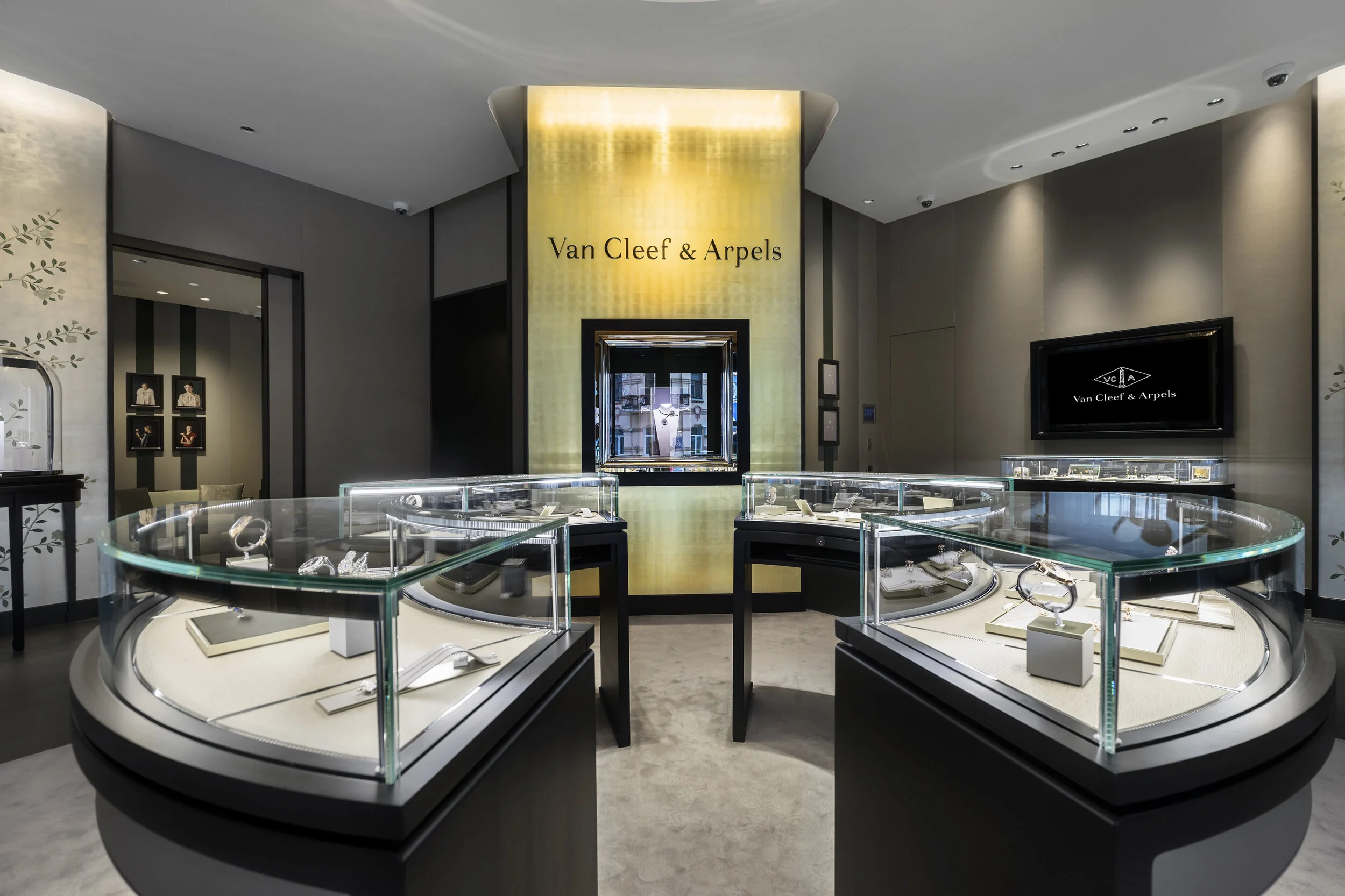 Luxury jewelry store interior with glass display cases, showcasing various high-end jewelry pieces, branded "Van Cleef & Arpels." The room features elegant lighting and decor, emphasizing a sophisticated and upscale ambiance.