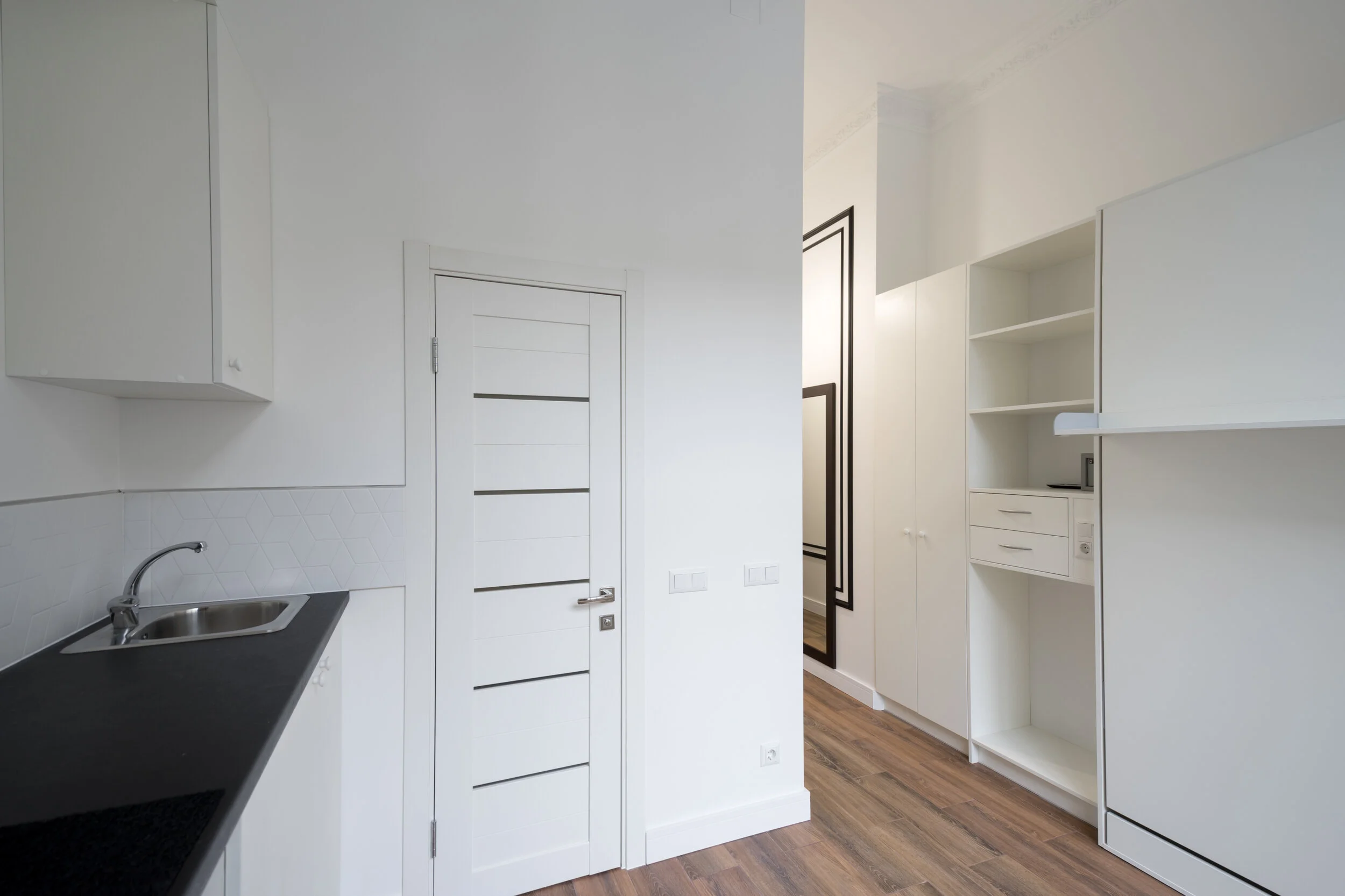 Modern minimalist kitchen with white cabinets, wood flooring, and a stainless steel sink.
