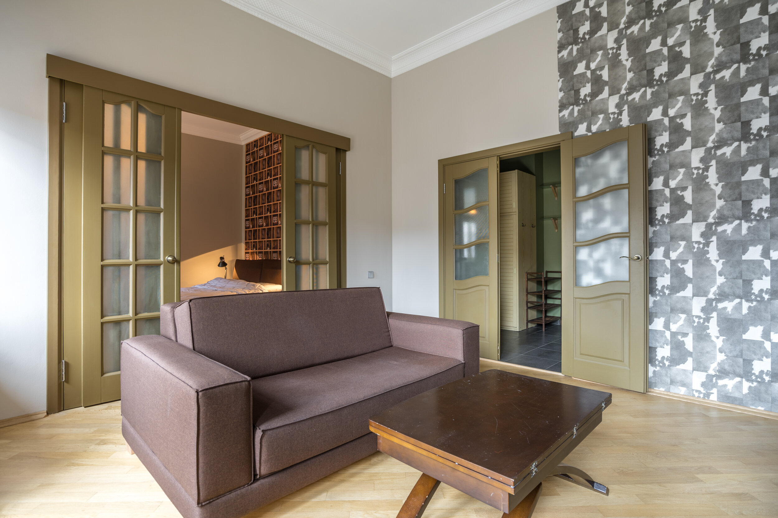 Living room with brown sofa, wooden coffee table, sliding doors leading to bedroom, and gray patterned accent wall.