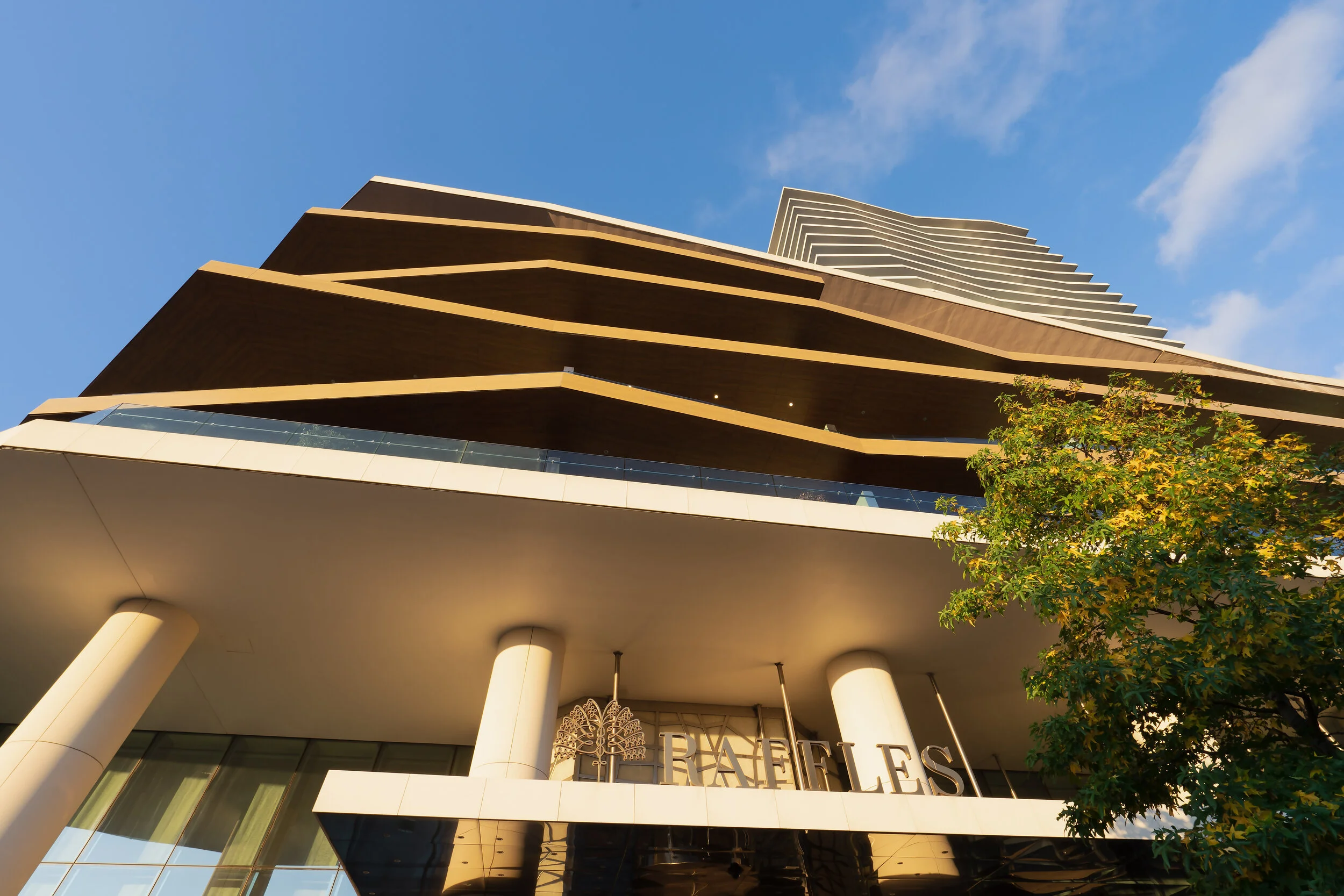 Modern high-rise building with angular design, labeled "Raffles," against a blue sky.