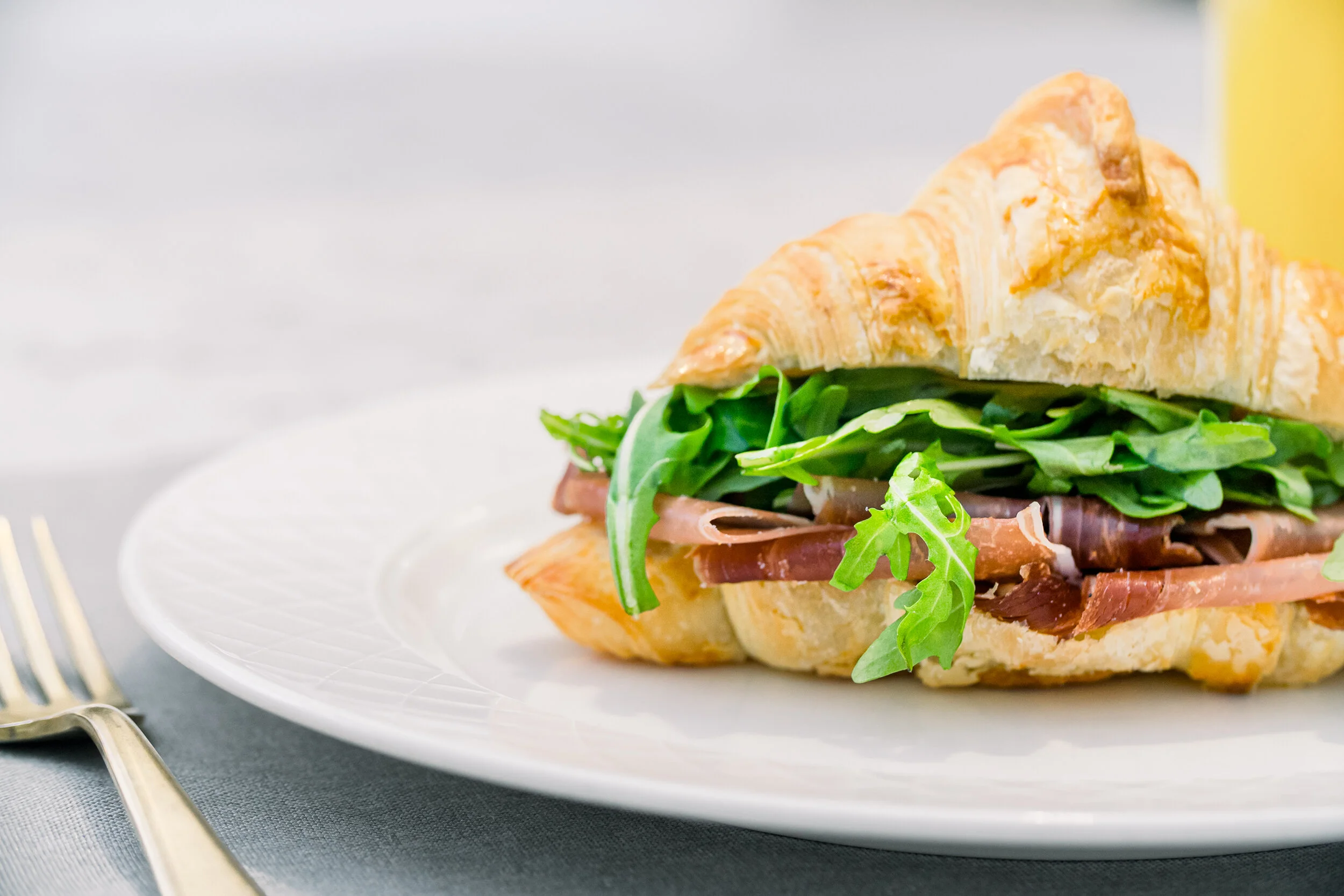 Croissant sandwich with prosciutto and arugula on a white plate.