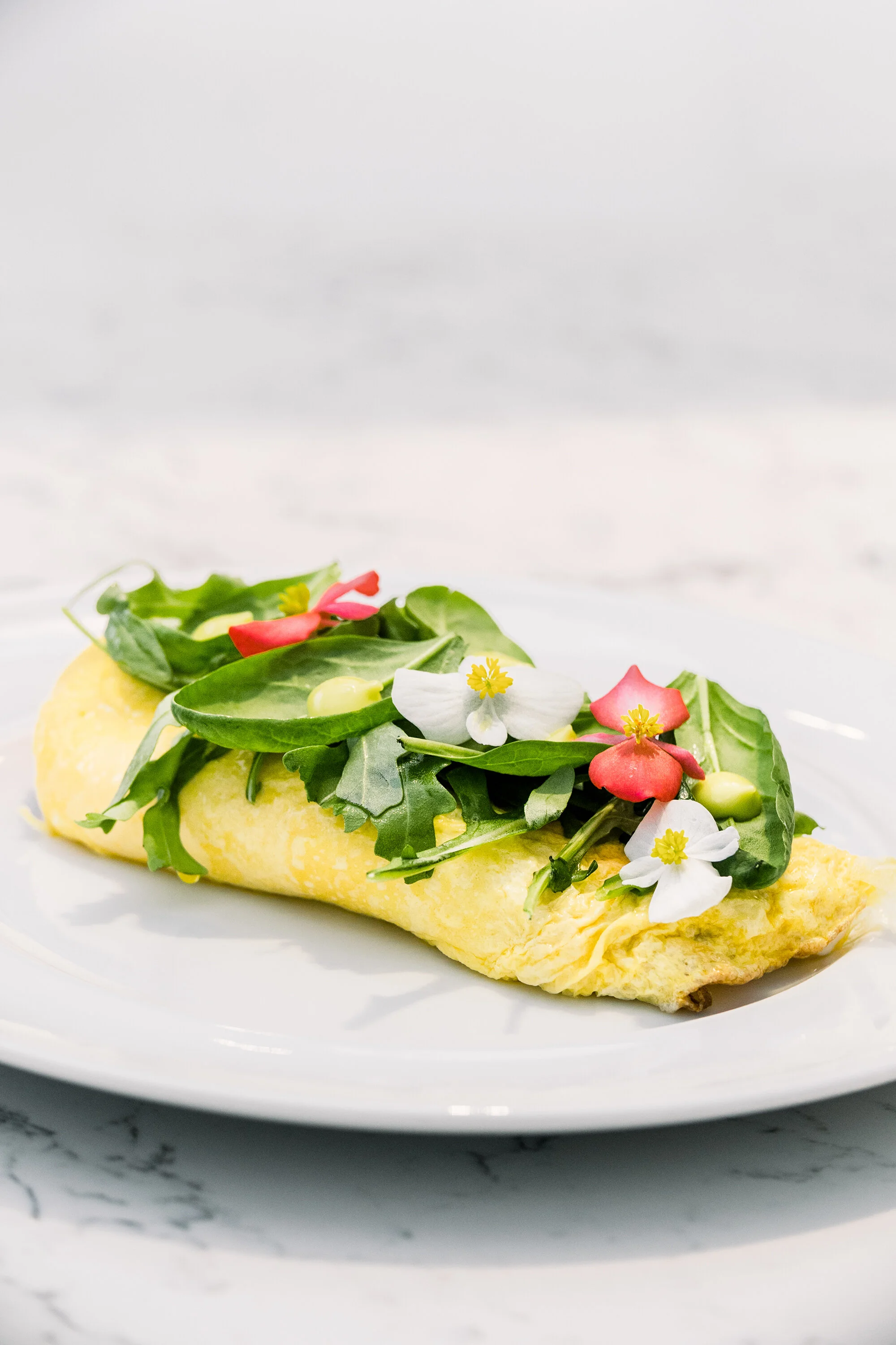 Omelette topped with arugula, edible flowers, and avocado on a white plate.