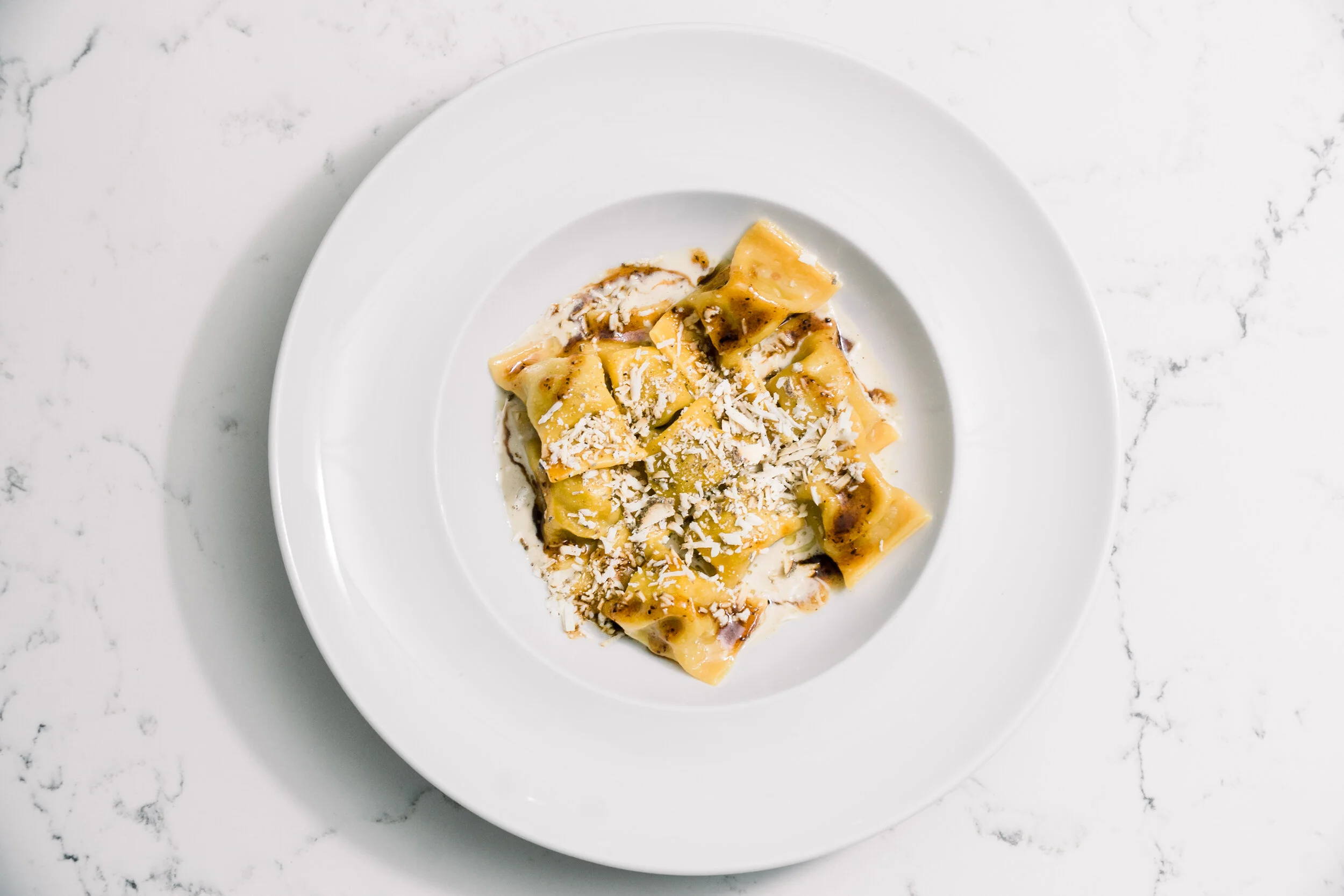 Plate of pasta with creamy sauce and shredded cheese on a white marble surface.