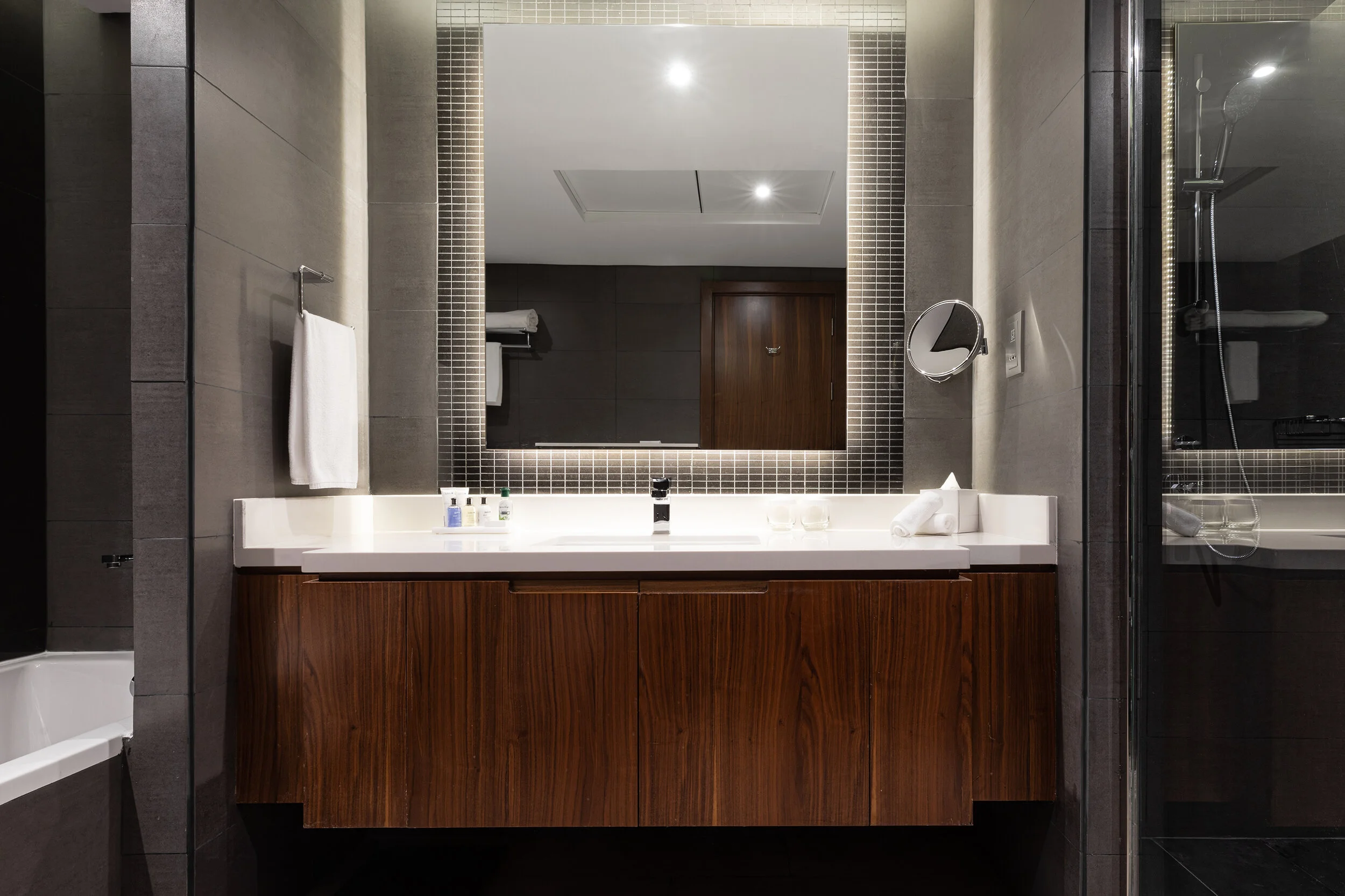 Modern bathroom with a large mirror, wooden vanity, gray tiles, and a walk-in shower.
