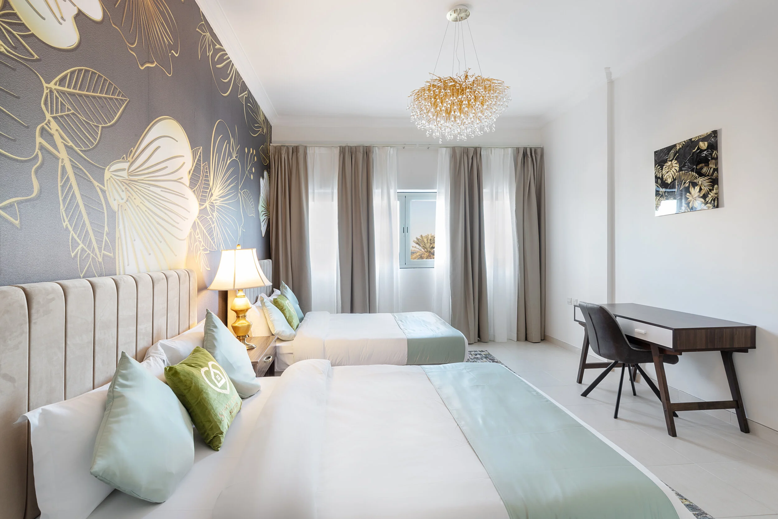 Elegant hotel room with two beds, decorative wallpaper, a modern chandelier, and a desk with a chair.