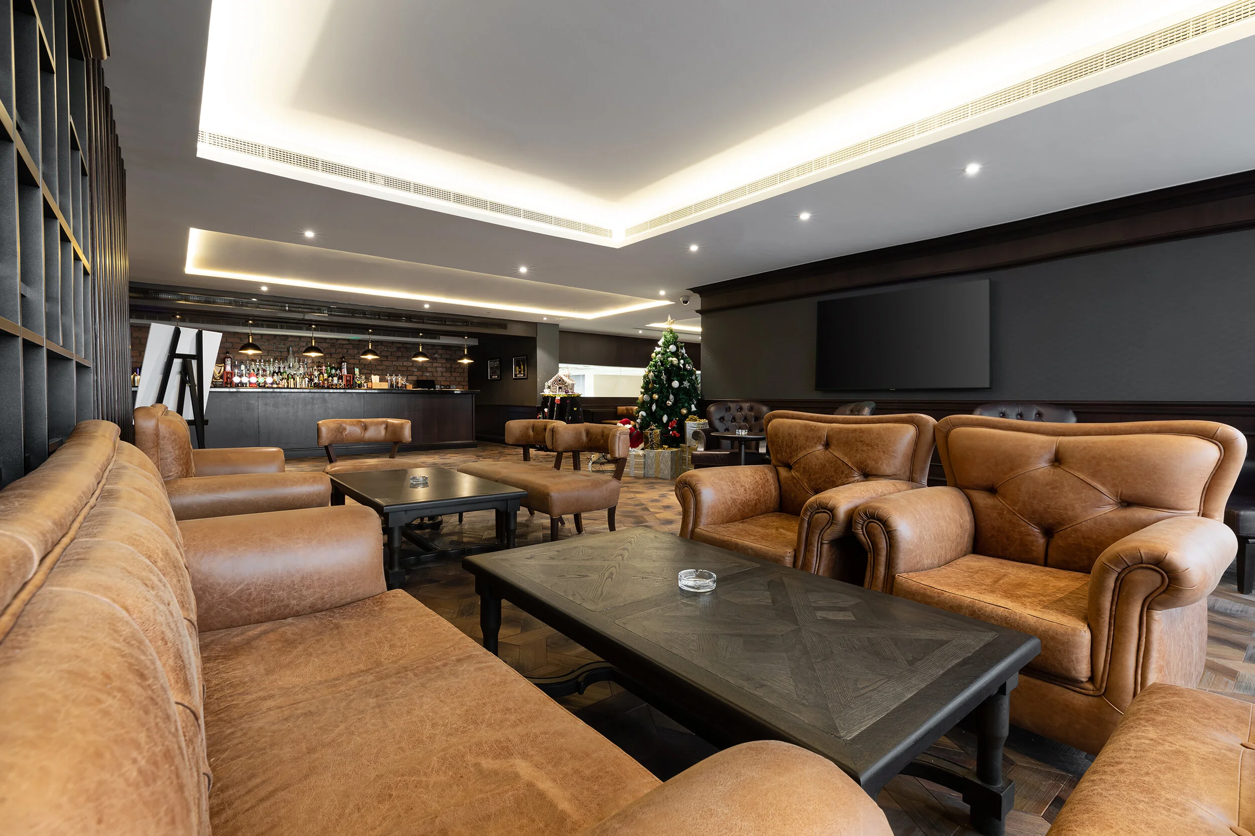 Luxury lounge with leather sofas, coffee tables, a bar area, and a decorated Christmas tree.