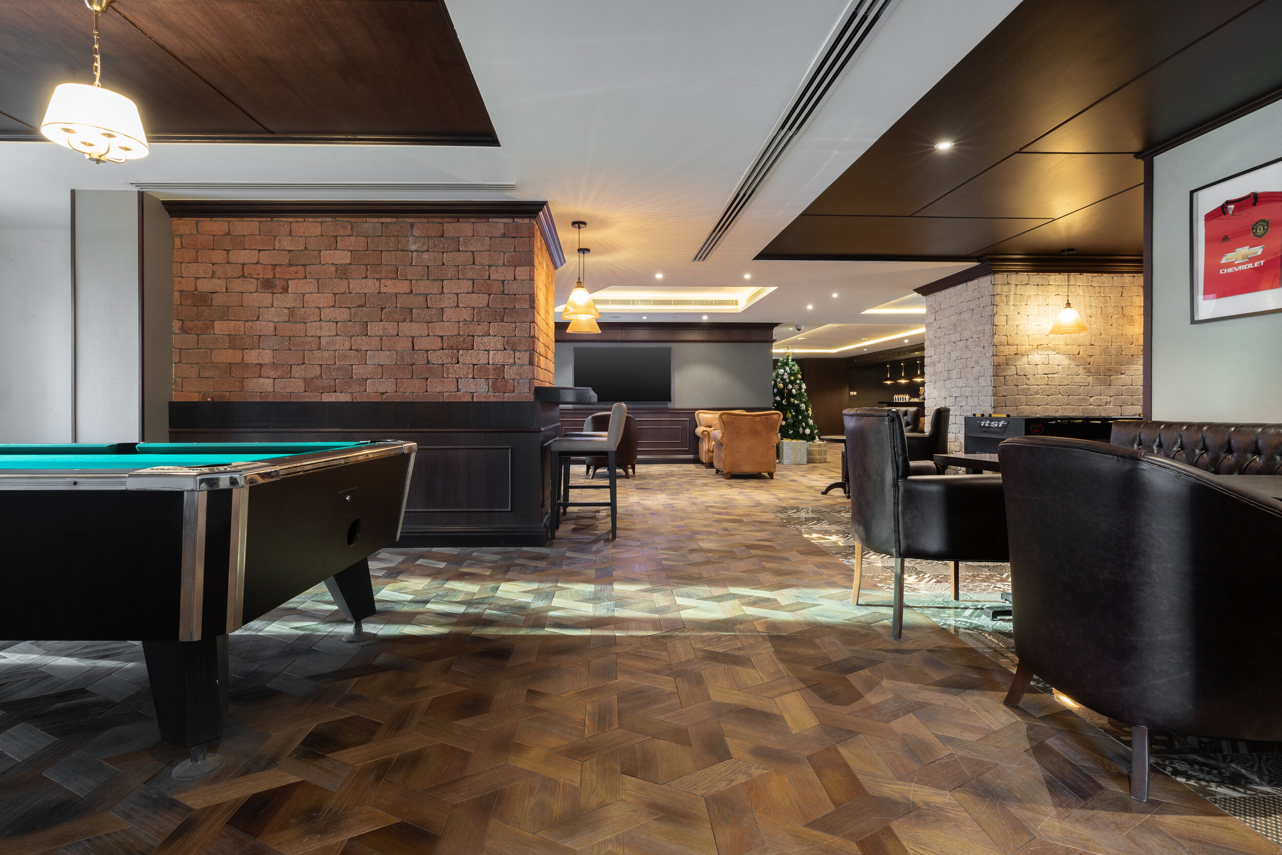 Interior of a modern lounge with pool table, leather chairs, brick walls, and a Christmas tree in the background.