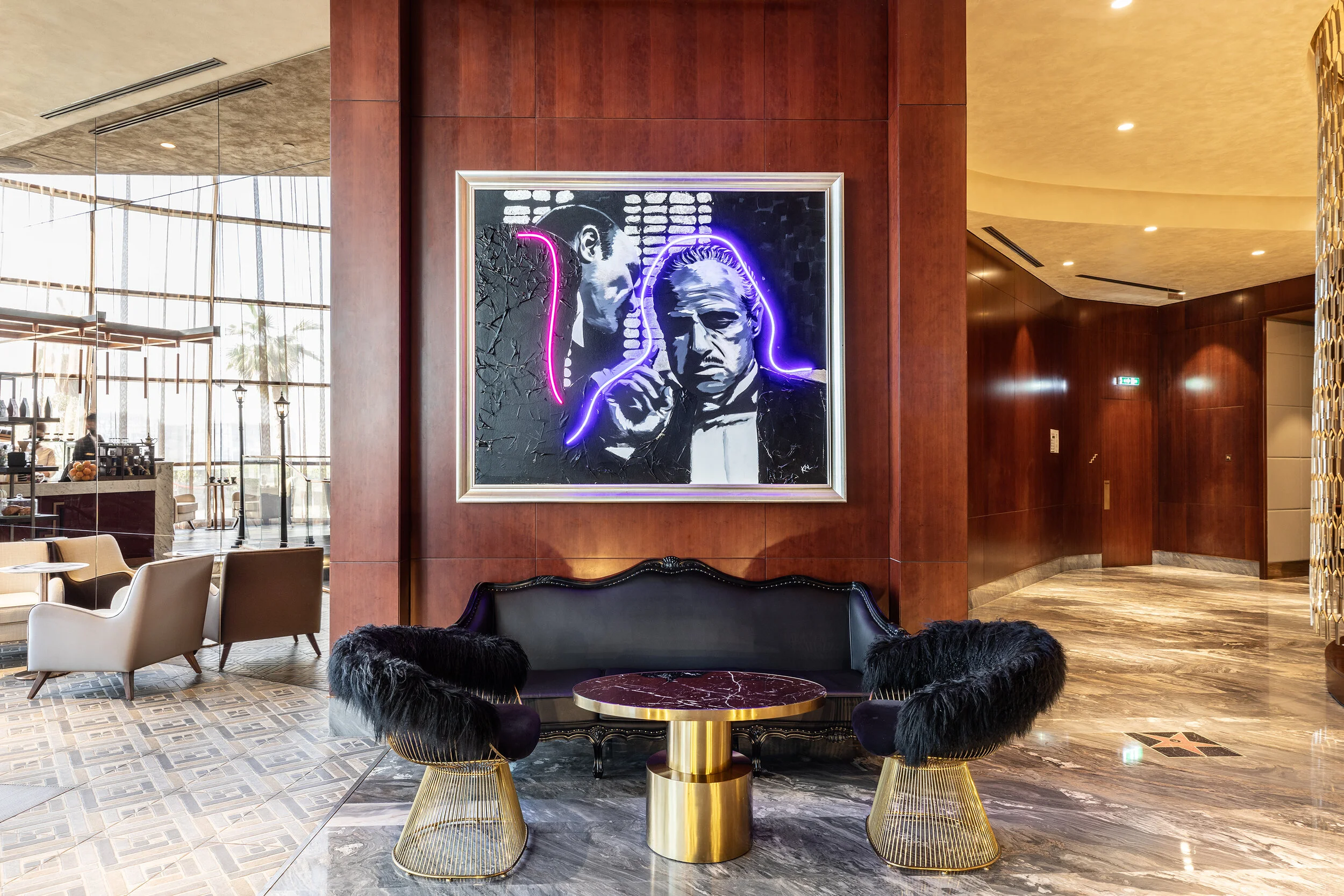 Interior of a stylish lounge area with modern furniture, featuring a large framed painting with neon lights on a wooden wall, marble floors, and elegant decor.
