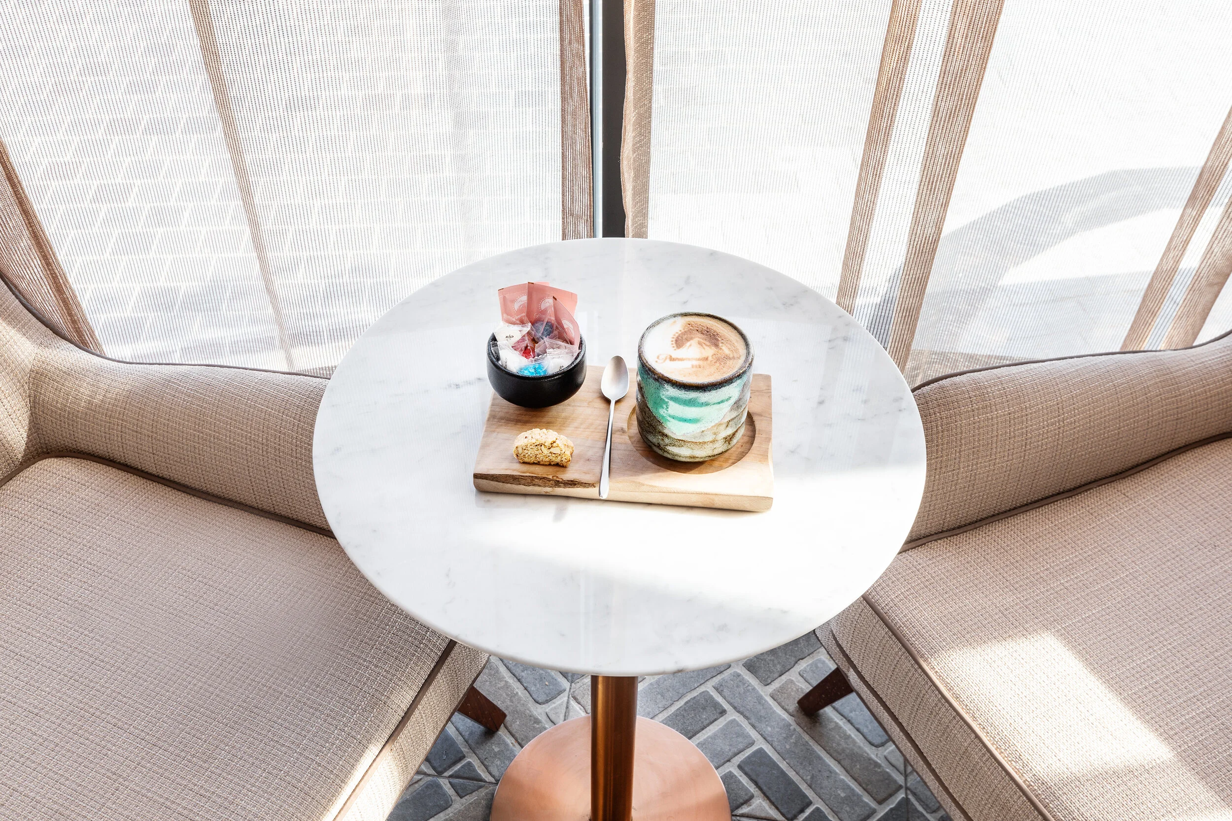 Table with a latte, cookie, candies, and spoon on a tray, surrounded by seating.