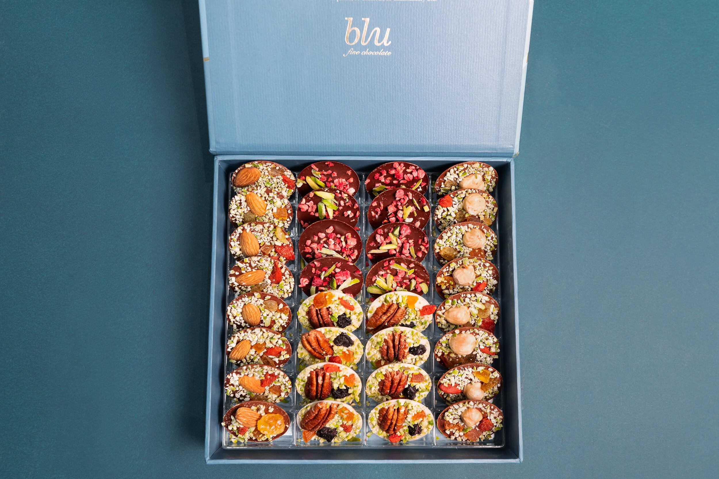 Open box of gourmet chocolates with nuts and dried fruits variety in a blue packaging.