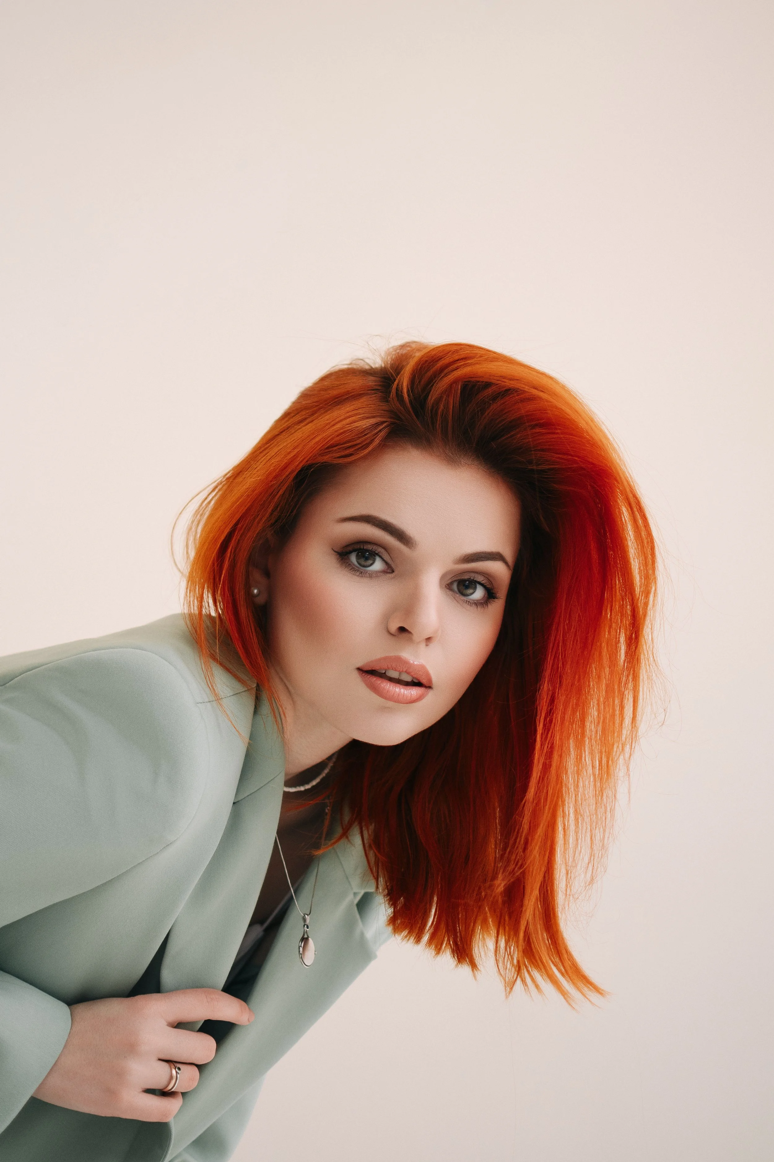Woman with bright red hair in a light green blazer, posing with a neutral background.
