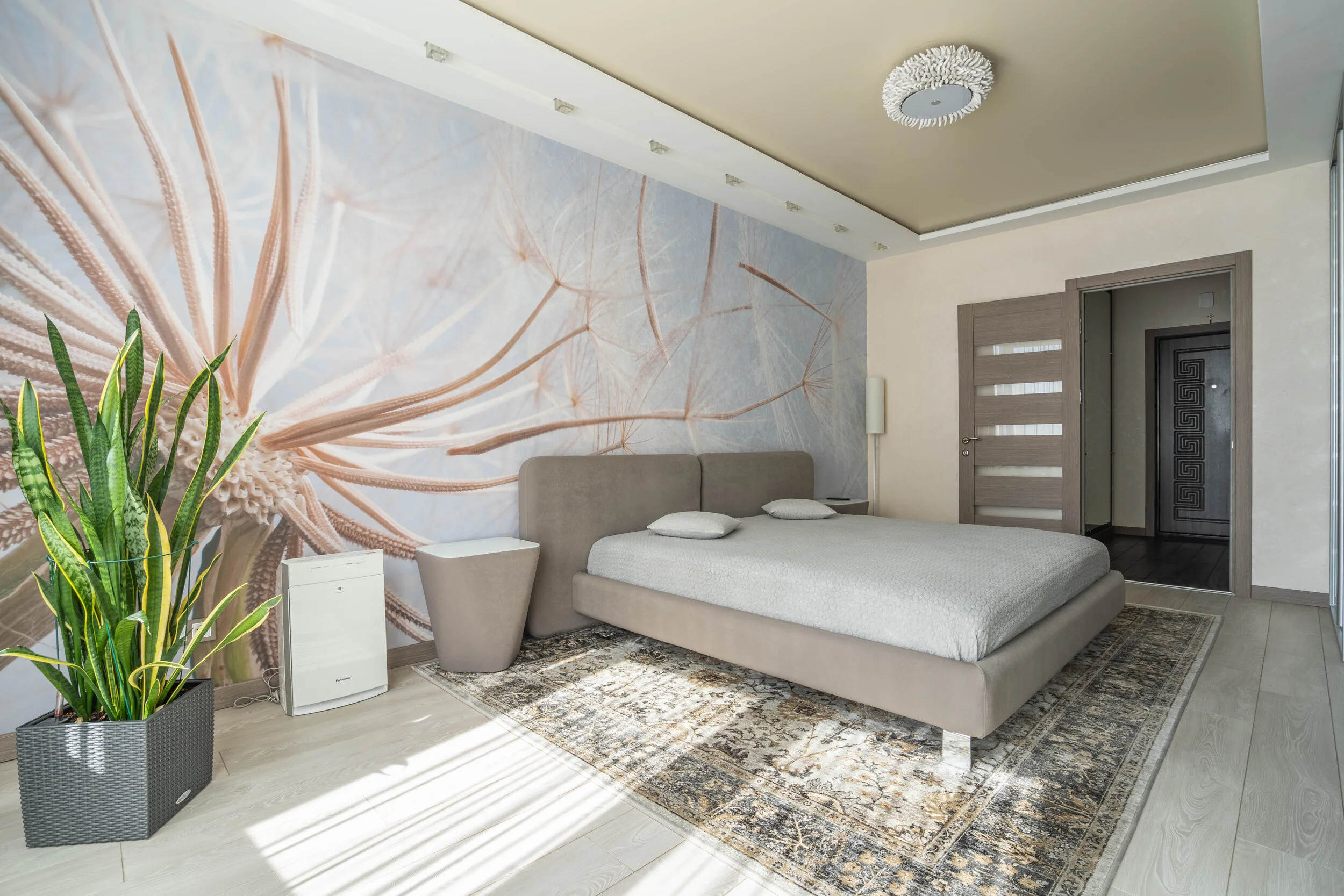 Modern bedroom with dandelion mural, gray bed, houseplant, air purifier, and patterned rug.