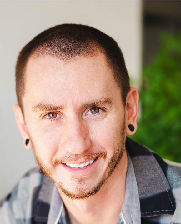Portrait of a man with short hair, wearing plug earrings and a plaid shirt, smiling at the camera.