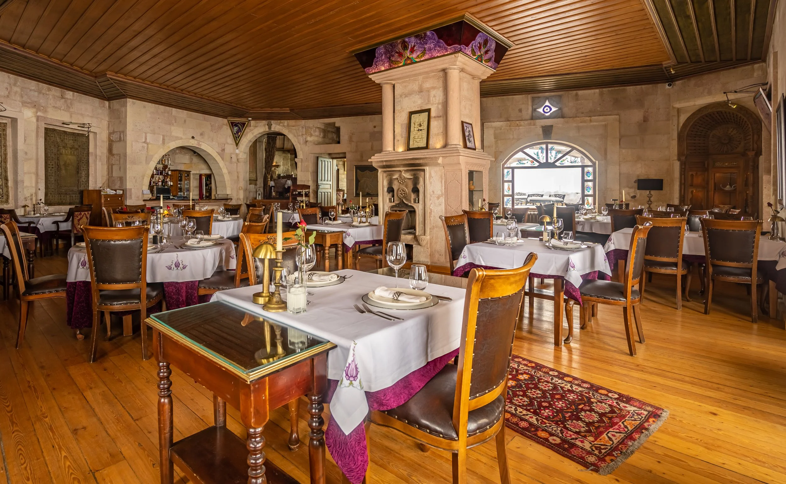 Elegant restaurant interior with wooden floors, stone walls, and tables set with white tablecloths and glassware.