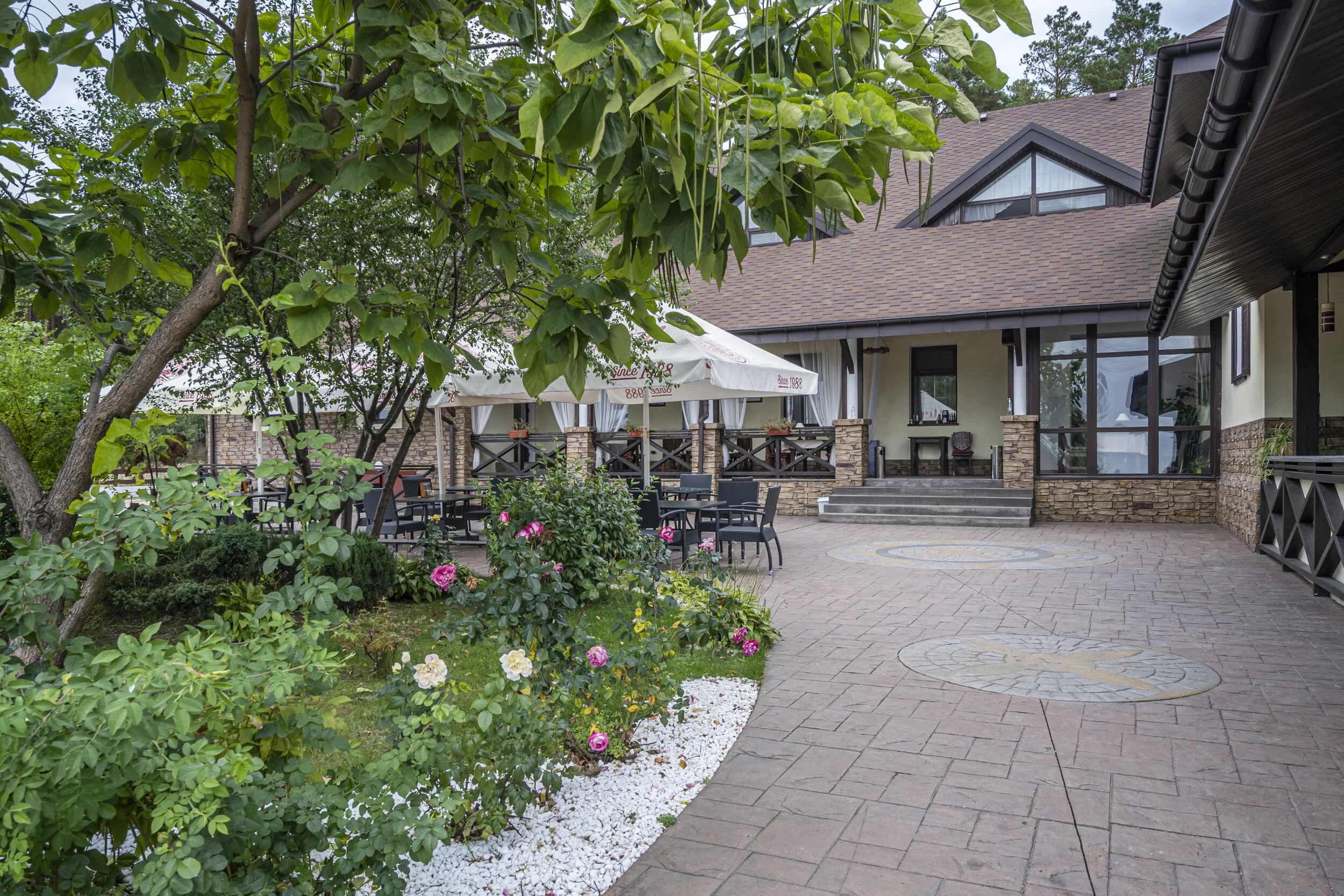 Outdoor patio of a restaurant with stone pathway, seating, garden, and canopy umbrellas.