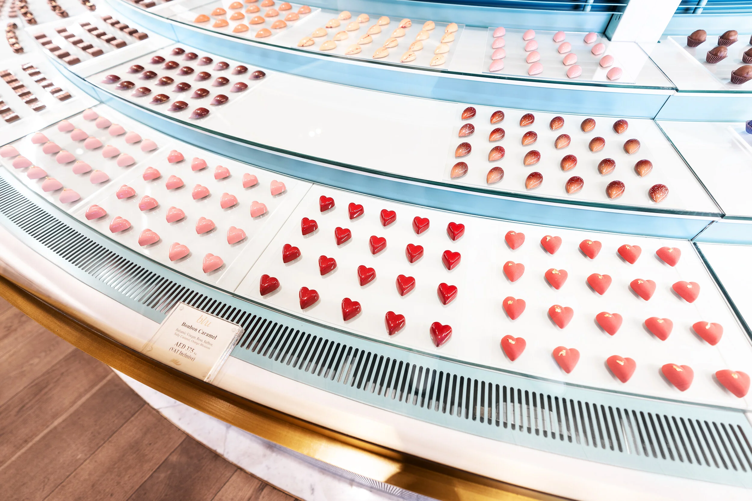 Display case with colorful heart-shaped chocolates arranged neatly in rows.