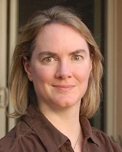 Woman with short blonde hair wearing a brown shirt