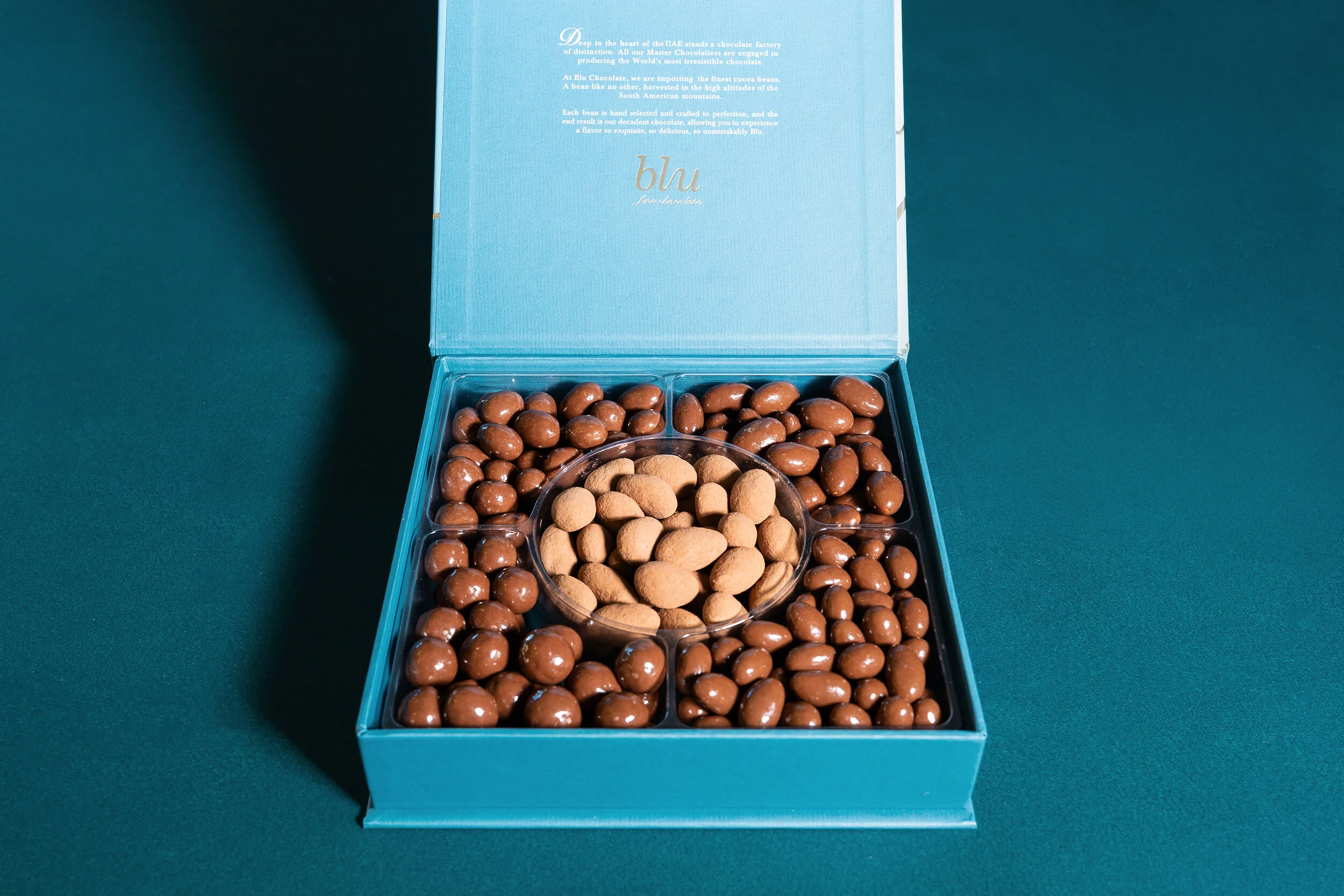 Box of assorted chocolates and nuts with a blue lid.