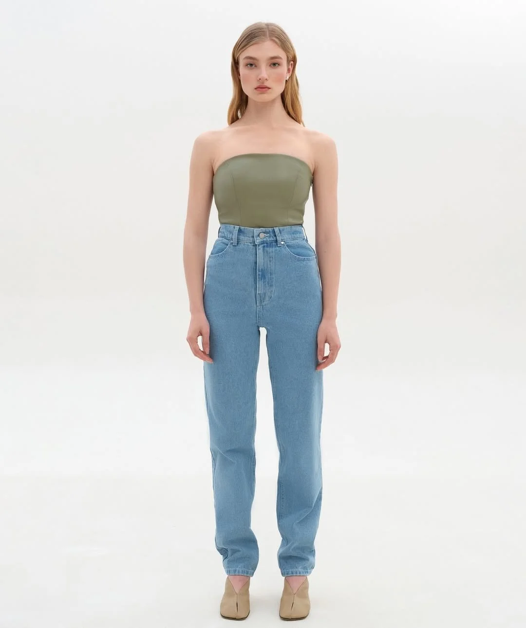 Woman wearing a strapless olive top and high-waisted blue jeans, standing against a white background.