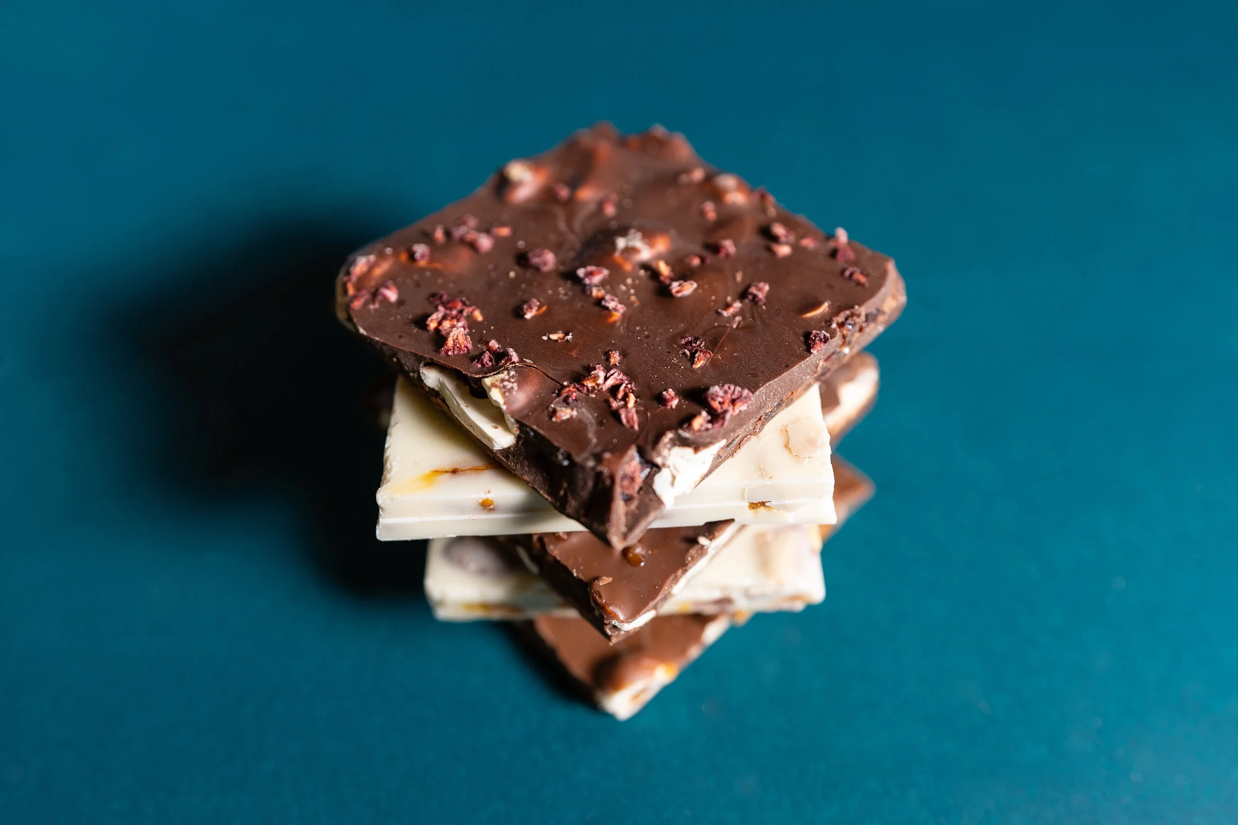 Stack of chocolate squares with various toppings on a blue background.