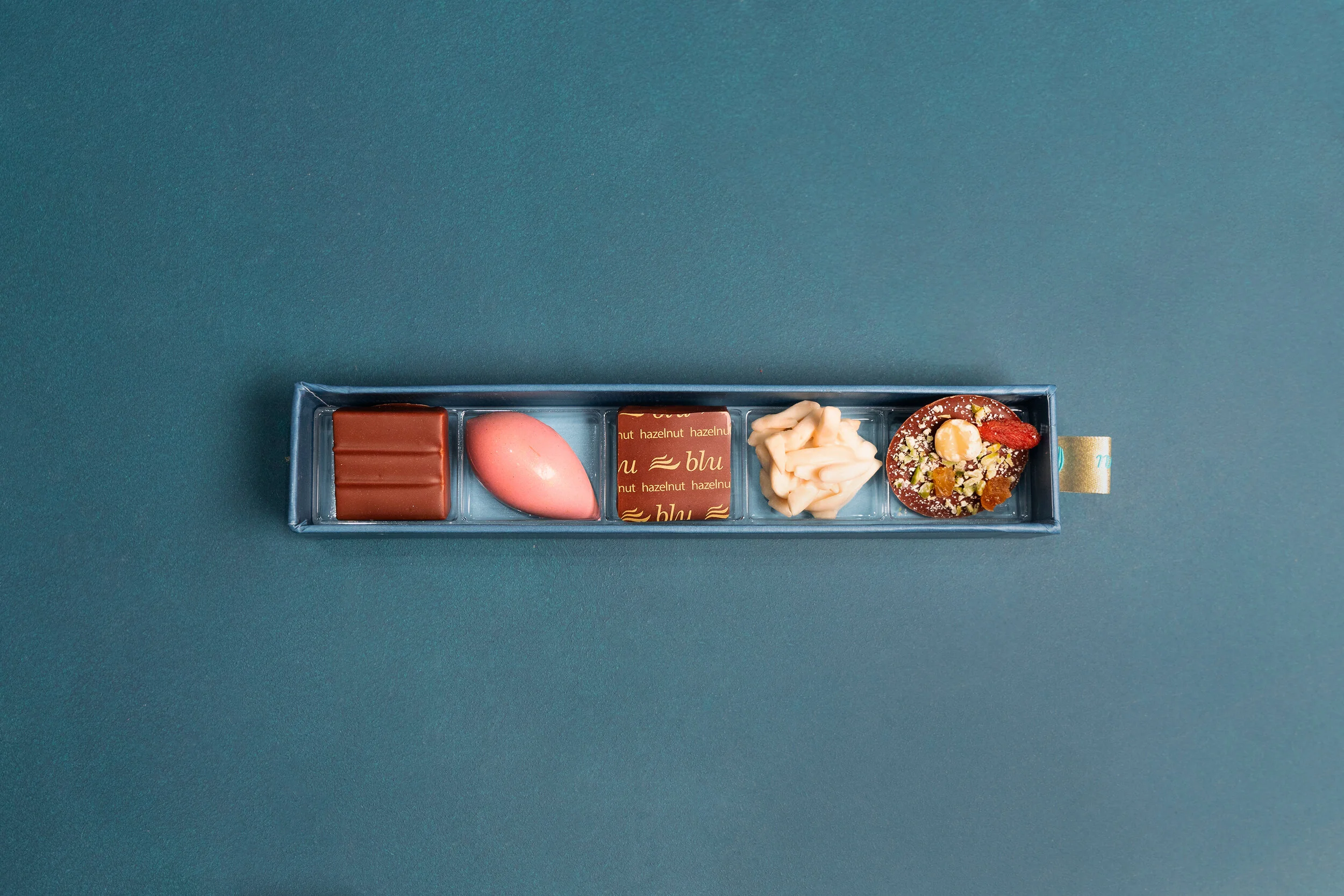A box containing five assorted chocolates on a blue background.