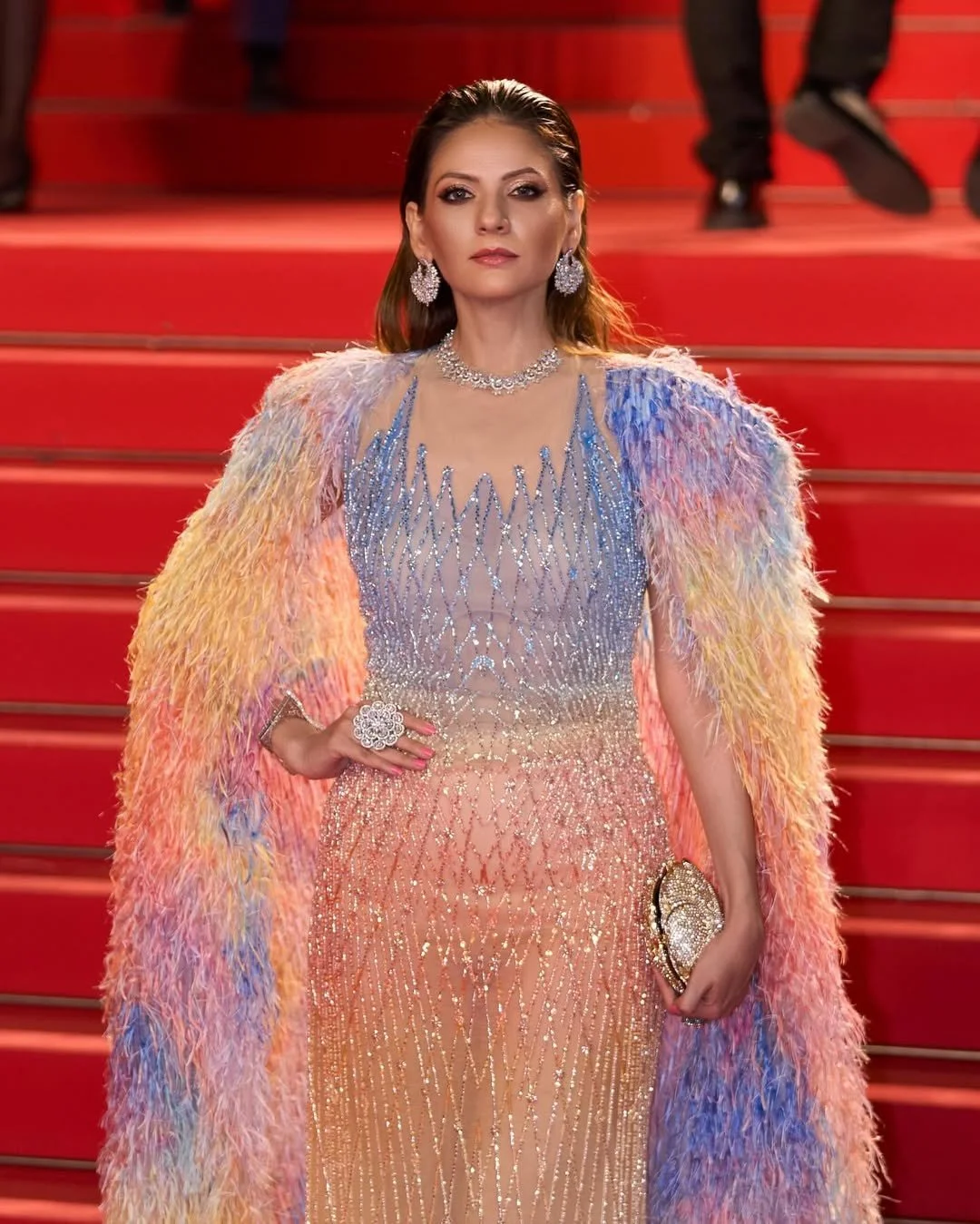 Person in a colorful, feathered gown on the red carpet.