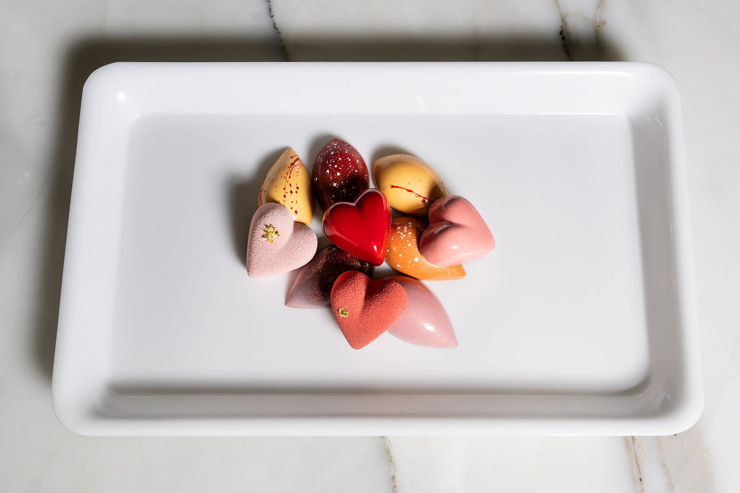 Assorted heart-shaped and oval chocolates on a white tray.