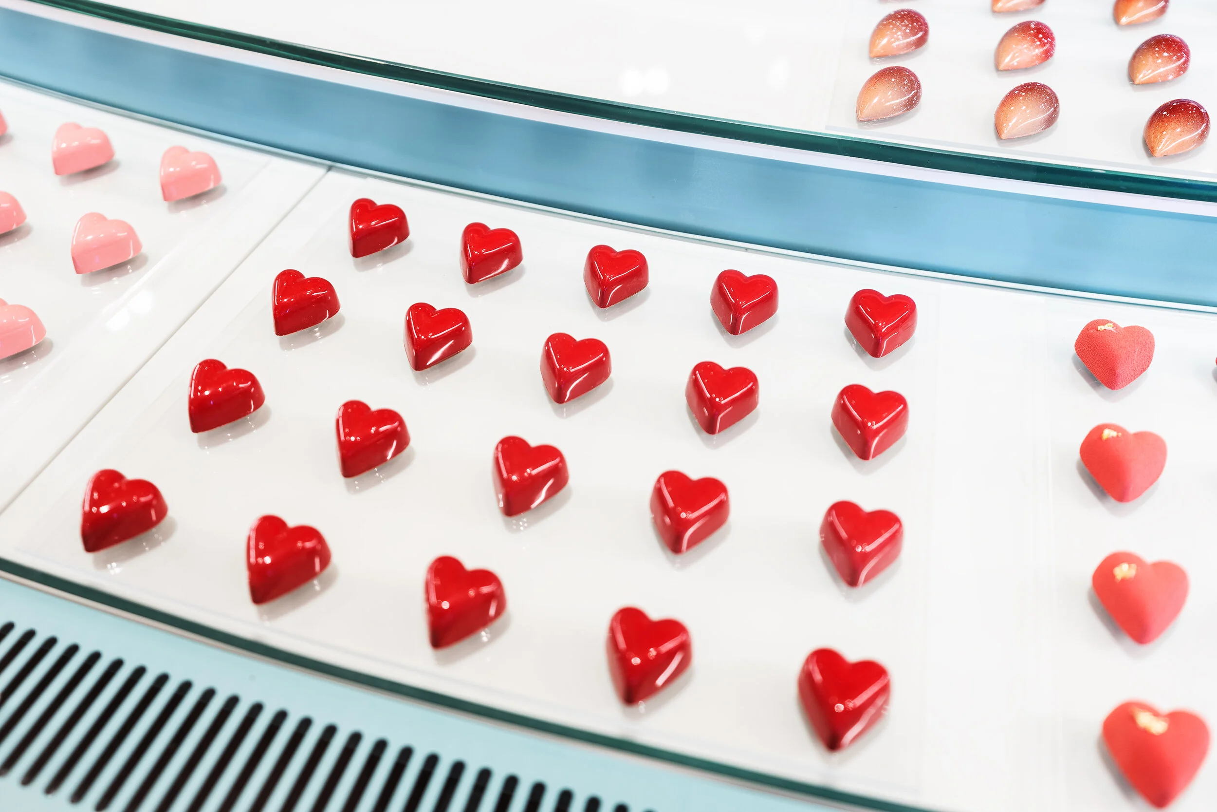 Heart-shaped chocolates in red and pink displayed in a glass case.