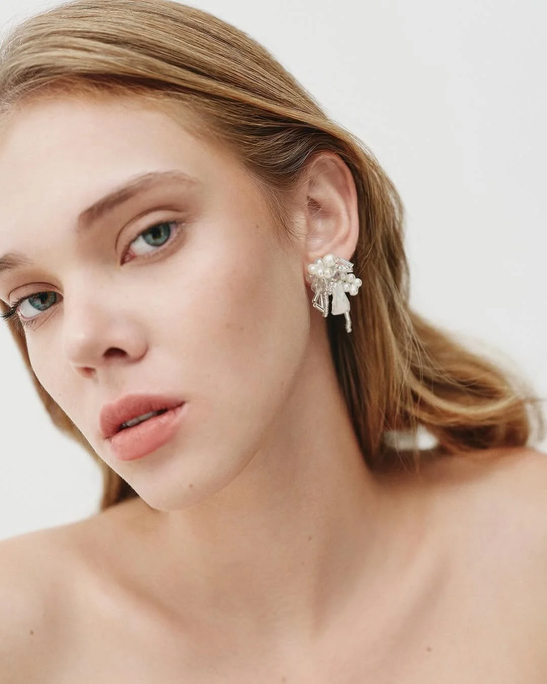 Close-up portrait of a person with light brown hair wearing decorative earrings on a white background.