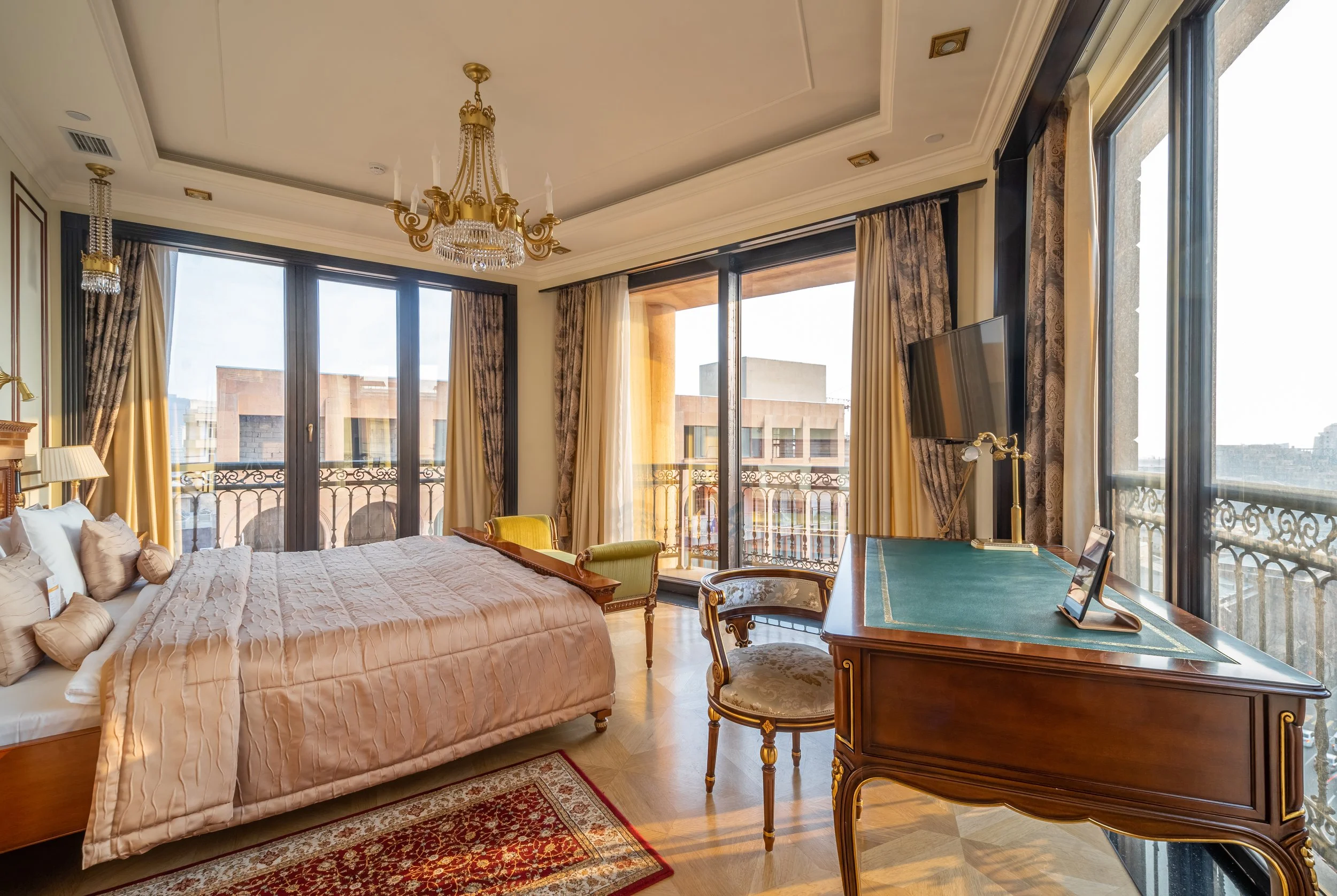 Luxurious bedroom with large windows, classic furniture, a chandelier, and elegant decor.