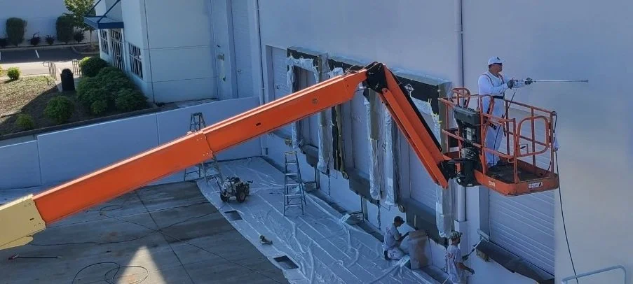 Commercial painting in Bellevue – painter spray coating a warehouse exterior from a boom lift