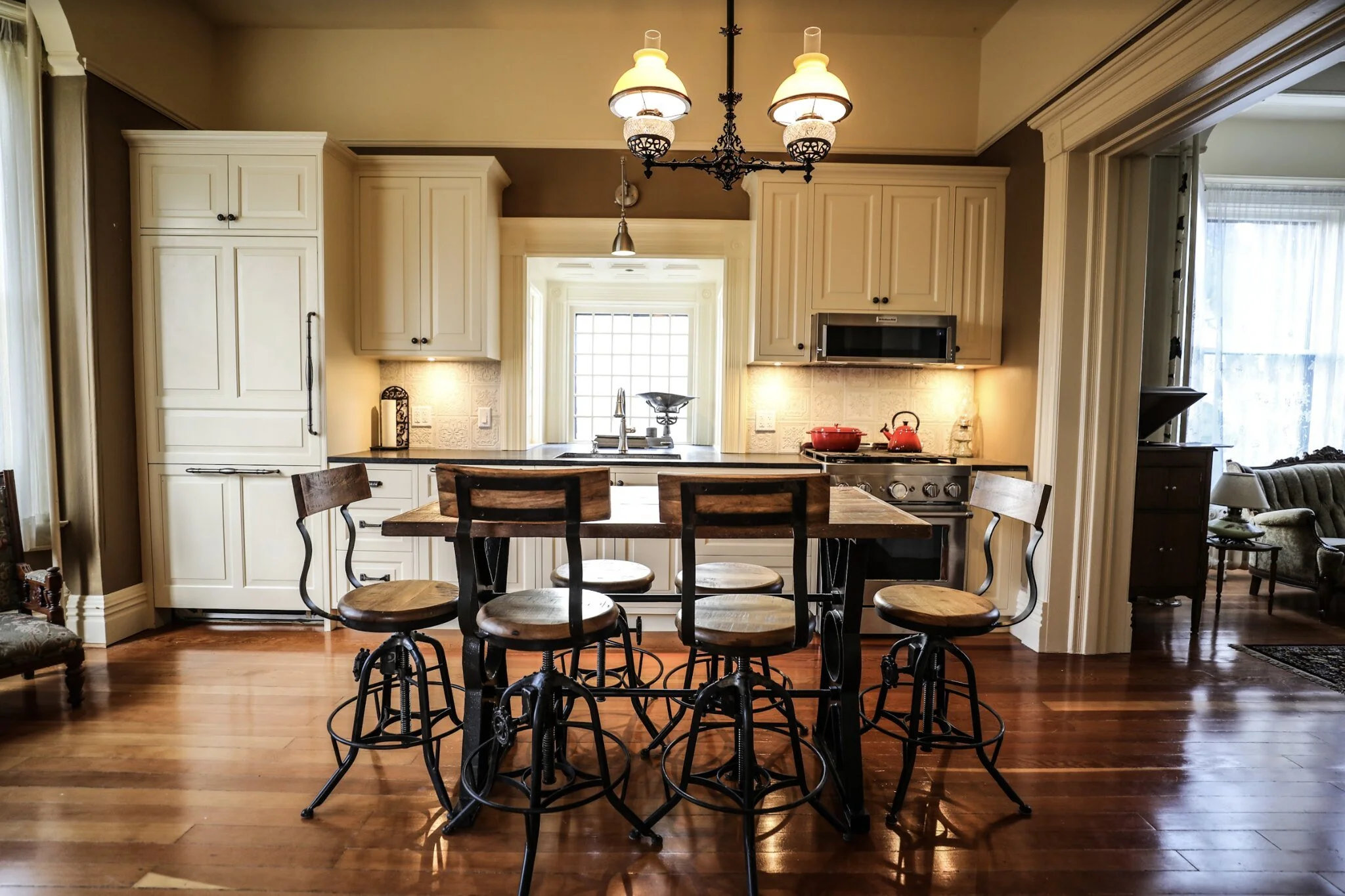 Guest Kitchen at The Wild Turkey Inn. View of a cozy kitchen with white cabinets, a central wooden island with four bar stools, black countertops, a stove, a window above the sink, and warm lighting.