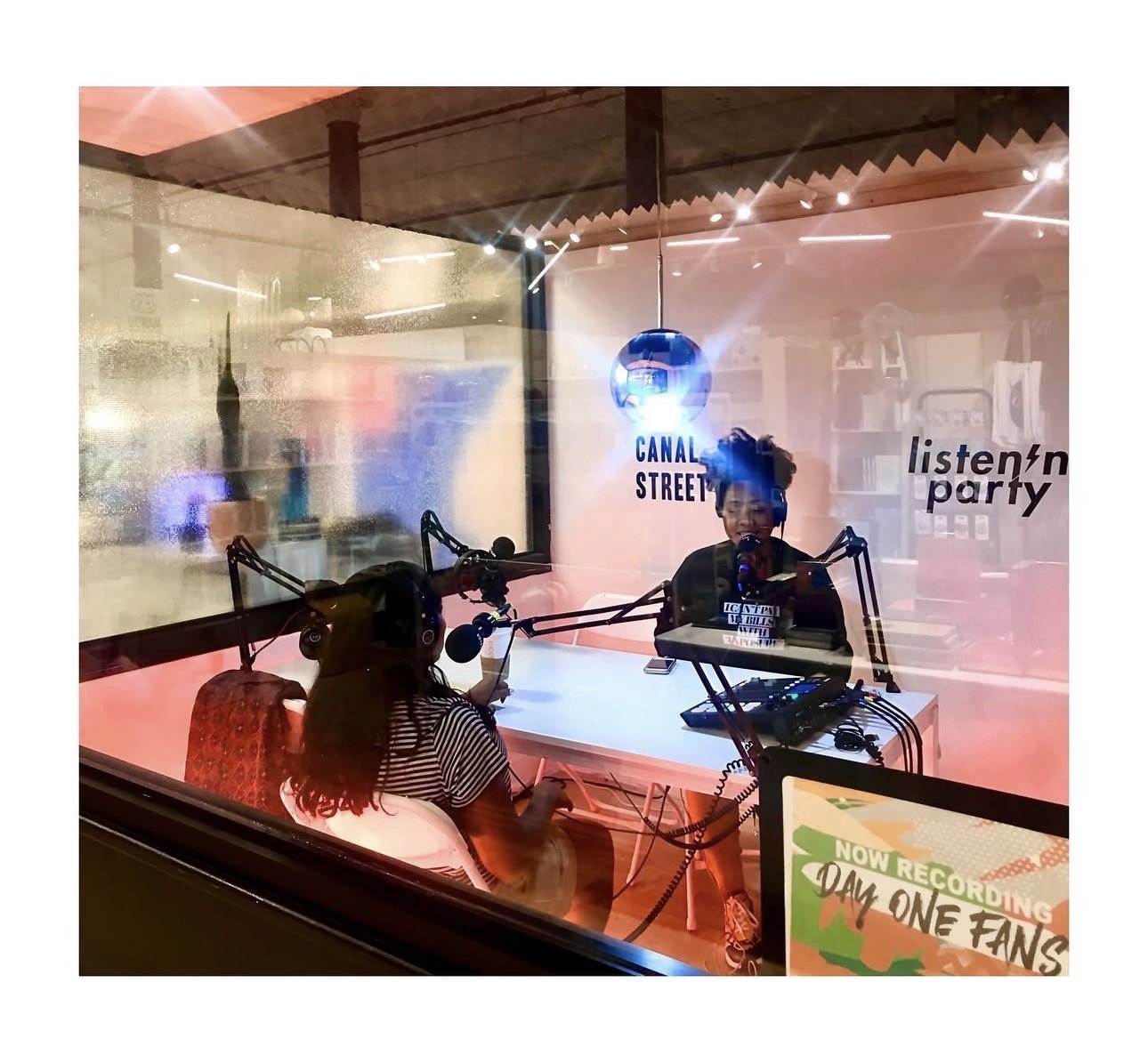 Radio station recording session with host Lachelle and Guest Marian at 'Canal Street' and 'listn'n party,' and a sign in the foreground indicating they are now recording for Day One Fans show.