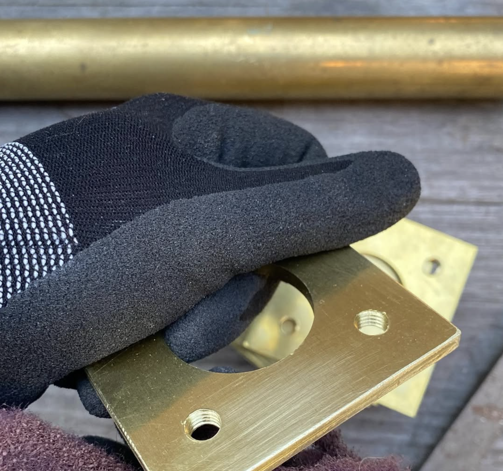 "Hands holding handmade brass letterbox component, showing precision metalwork and tapped fixings"