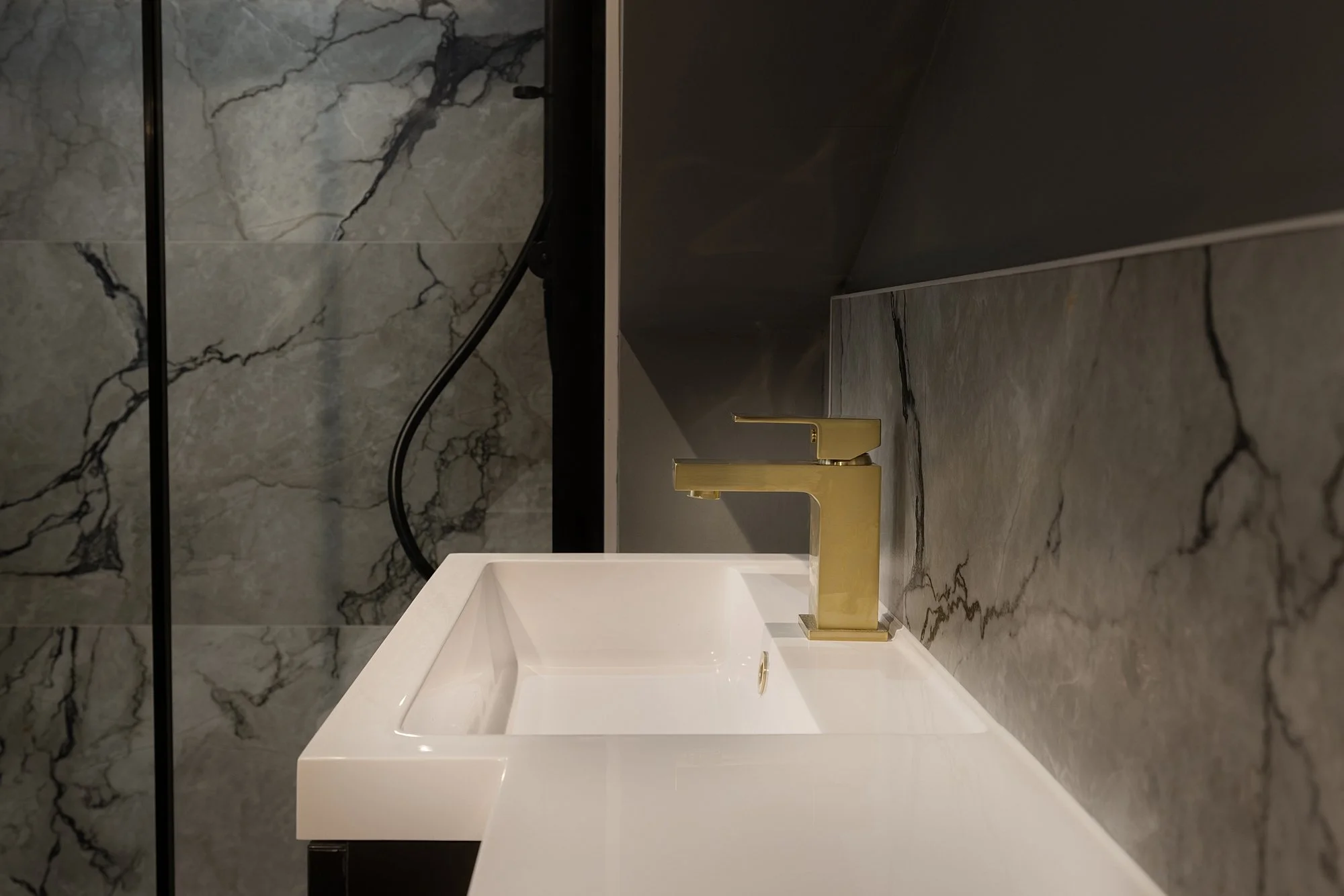 A modern bathroom sink with a gold faucet, set against a marble countertop and matching marble wall tiles.