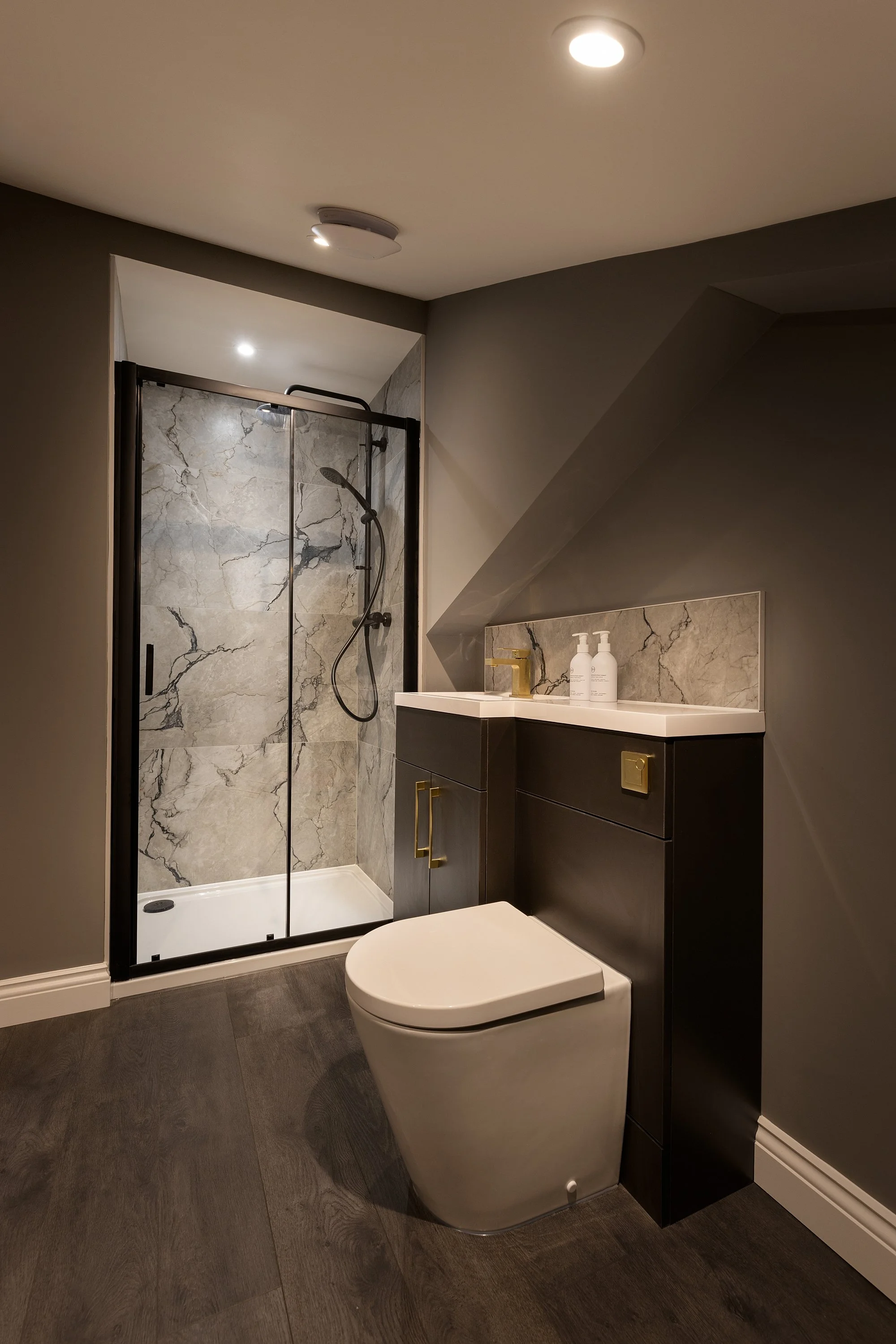 Modern bathroom with a glass shower enclosure, a white toilet, and a black vanity with gold handles and a marble countertop.