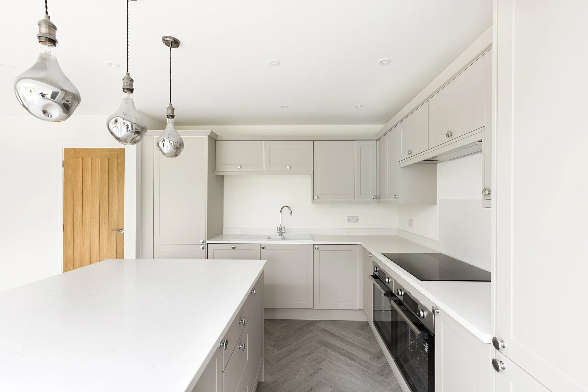 Modern white kitchen with hanging pendant lights, cabinetry, an oven, and a marble countertop island.