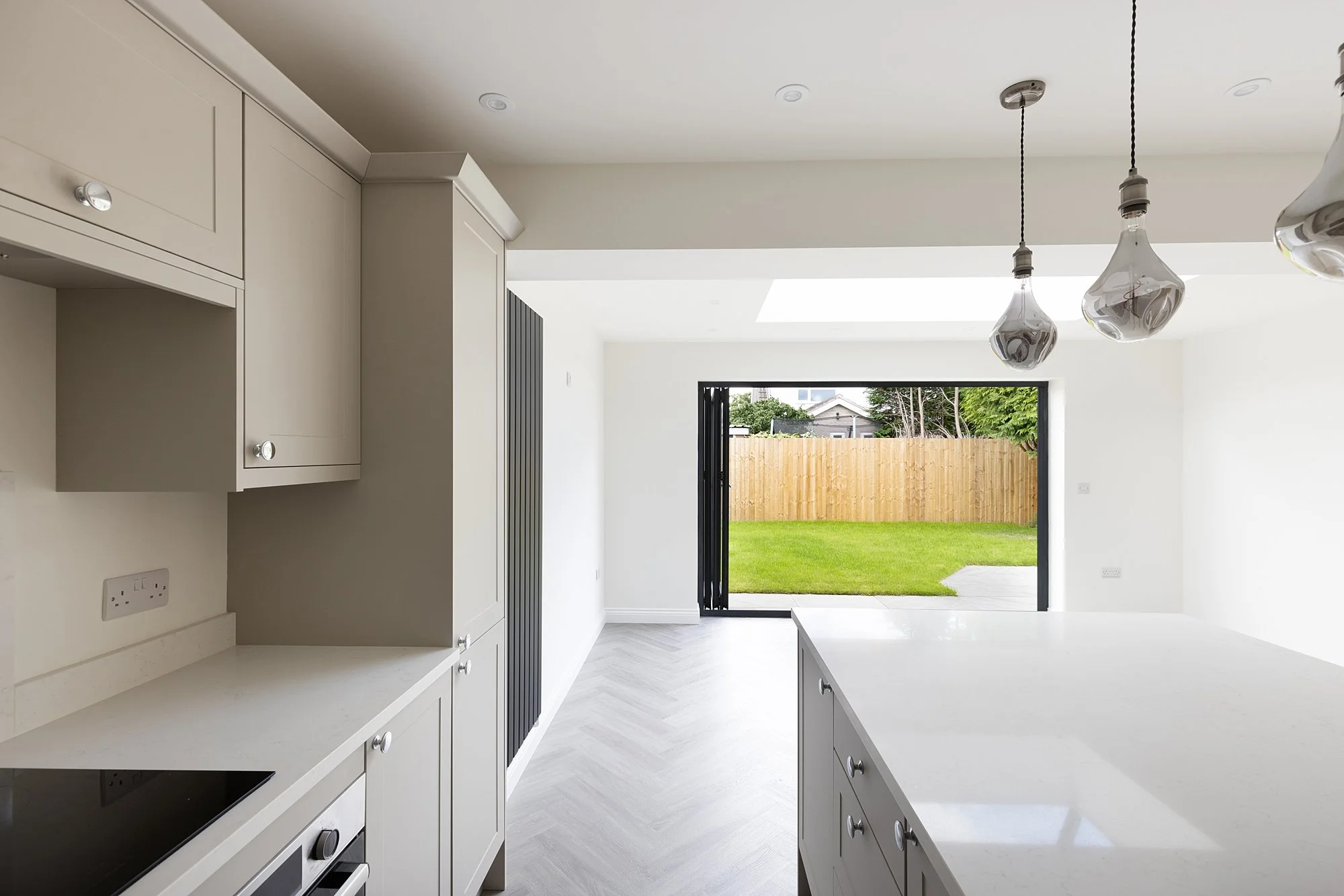 Modern kitchen with white cabinetry, a large island, pendant lights, and a view of a backyard with green grass and a wooden fence.