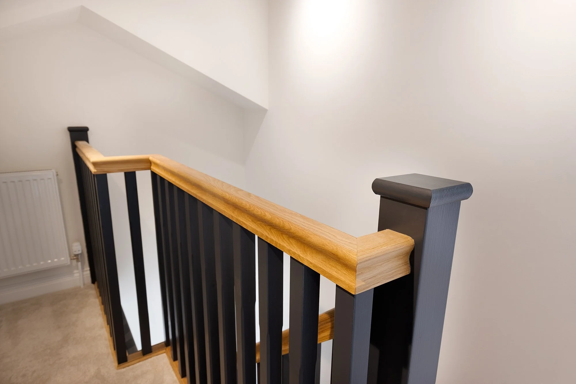 Indoor staircase with black balusters, a natural wood handrail, and a white wall background.