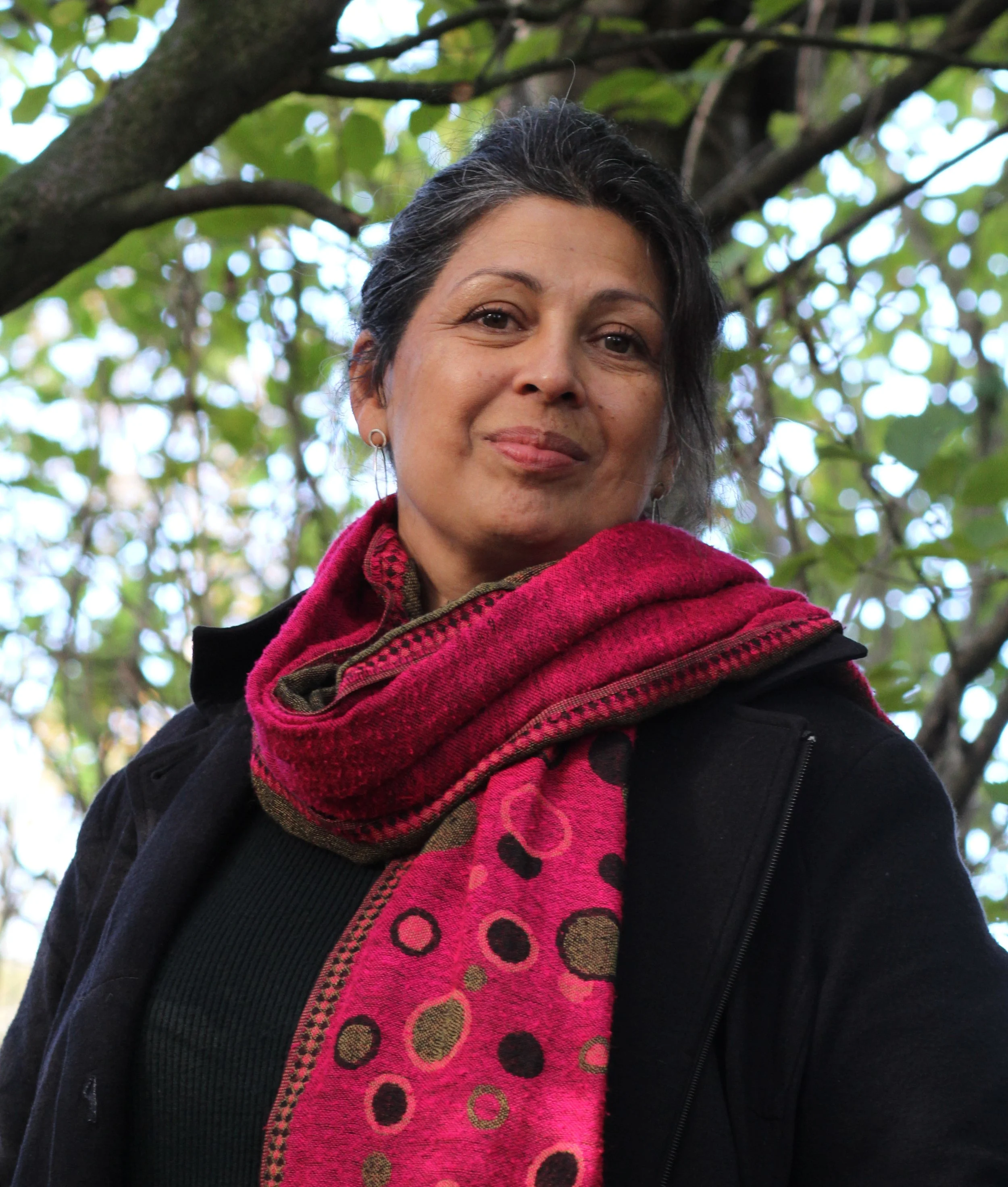 portrait photograph of sita brahmachari in coat and pink scarf with tree behind