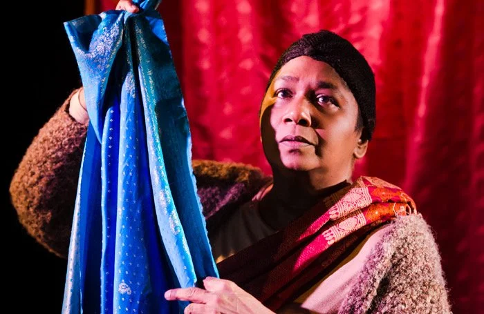 still photo from stage production of whose sari now a woman holds a length of blue sari cloth