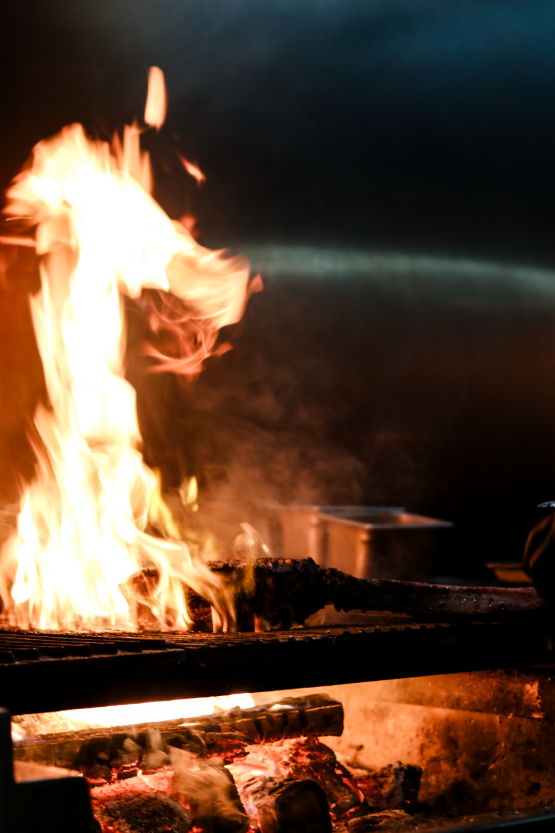 Fire burning on a grill with glowing coals underneath, with a dark background.