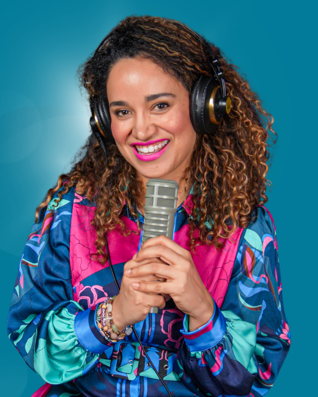 Woman with headphones holding a microphone, wearing a colorful patterned blouse, smiling against a blue background.