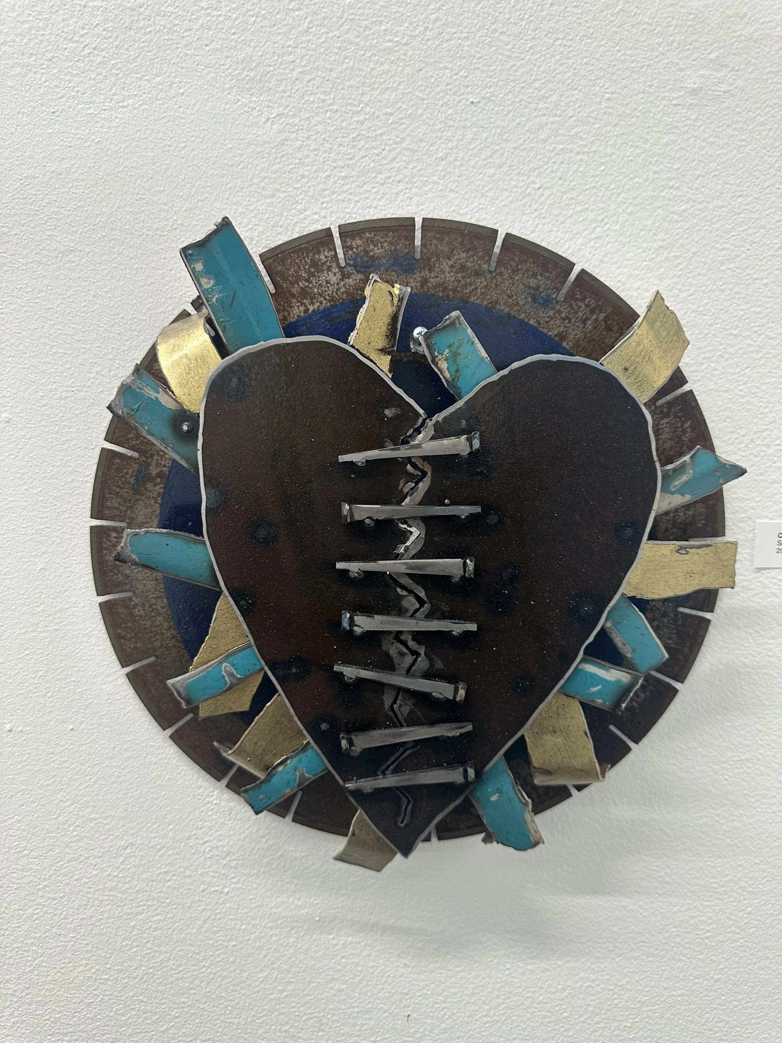 Mixed media art clock with a cracked heart shape in the center, on a white wall.