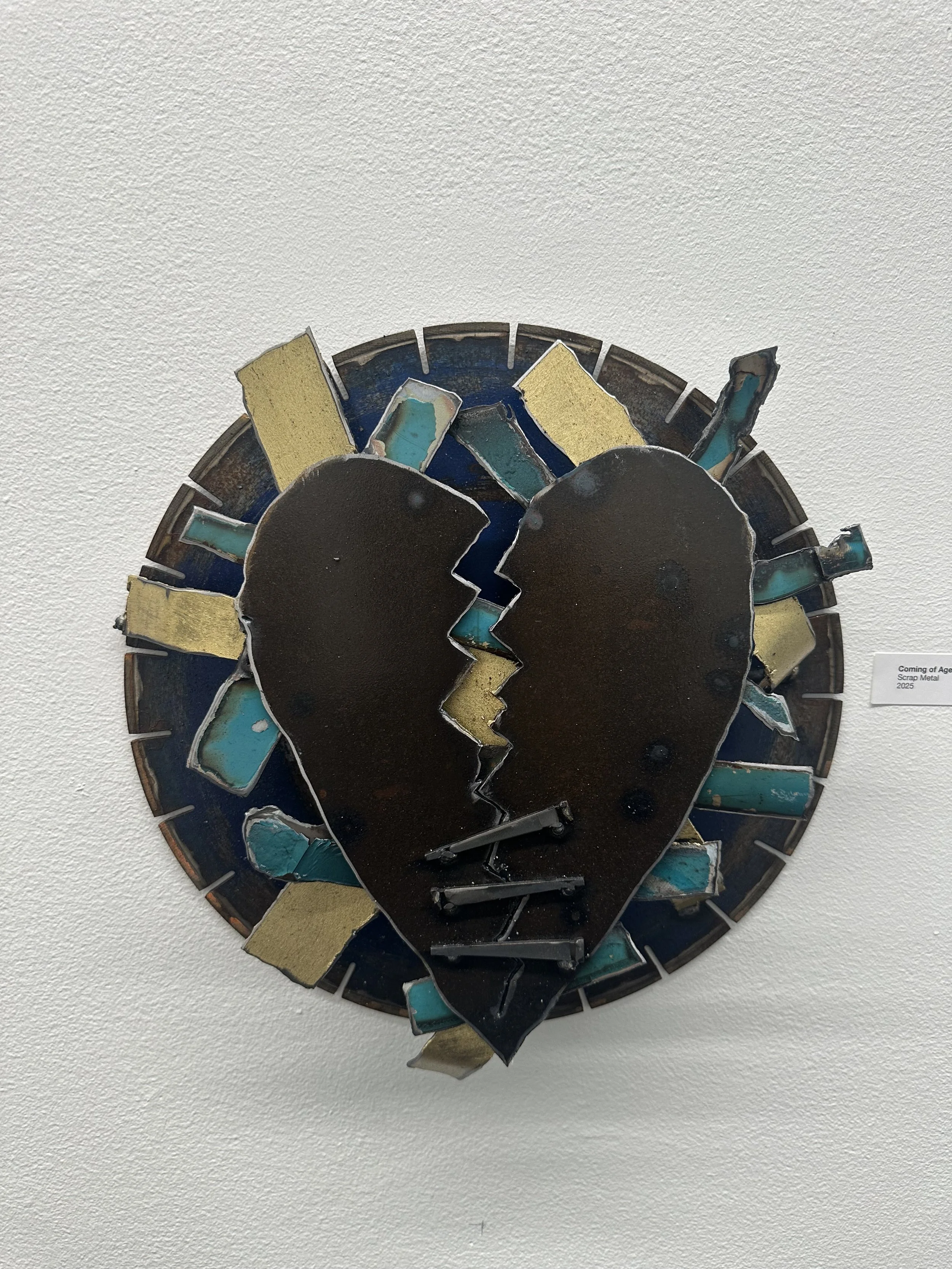 A metal artwork depicting two broken faces in profile, positioned to form a heart shape, with various colored metal pieces around them.